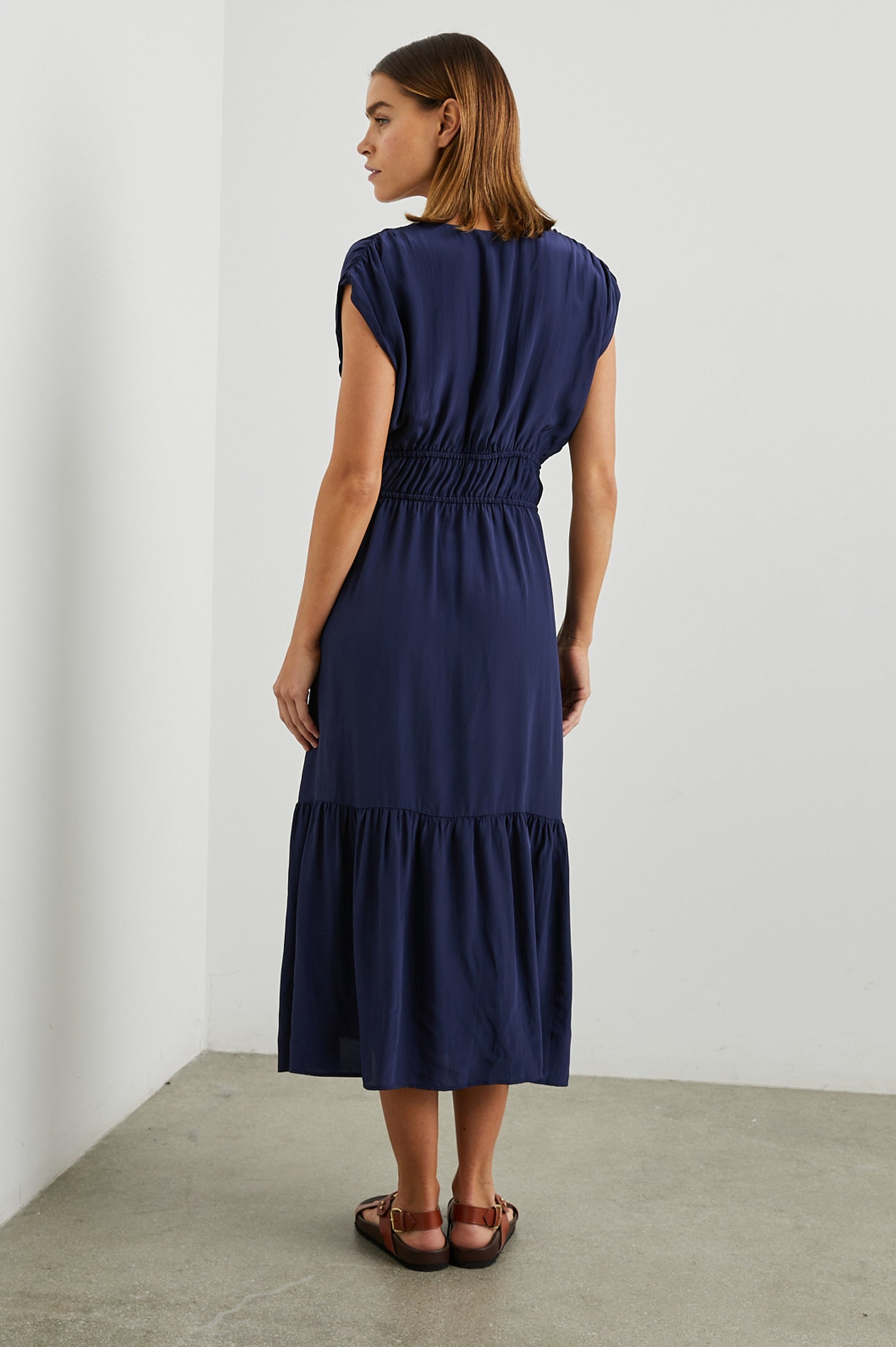 Aletta Short Sleeve Midi Dress with Cap Sleeves with Wide Arm Holes, Two Drawstrings at the Waist, a Deep V Neck, a Tiered Skirt and Ruching at the Front Yoke Seam and Shoulder Seam in Admiral Blue Colorway - Back Full Body View Featured on Model