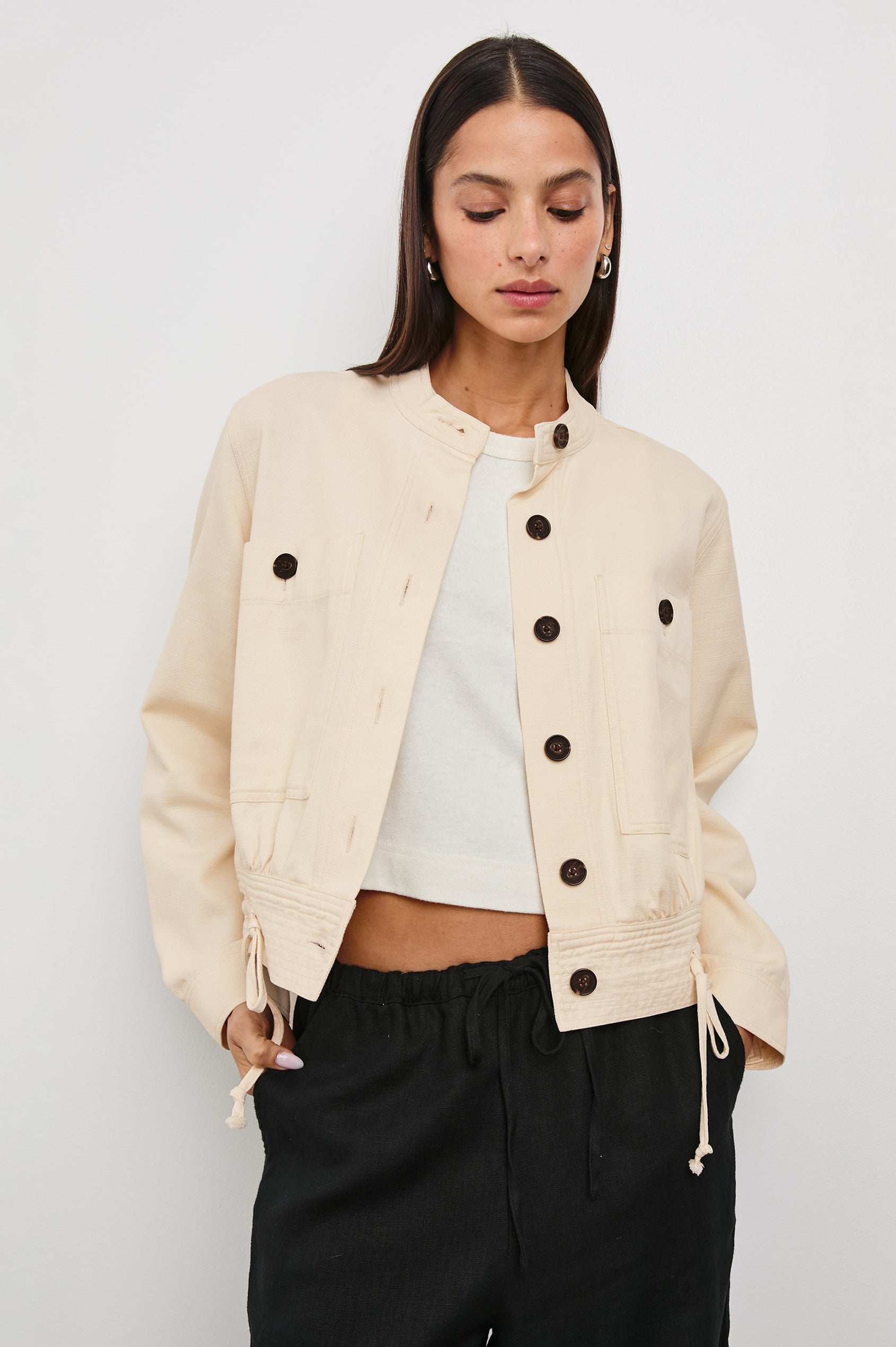Alma Jacket with Button Closure, Mandarin Collar, Two Large Chest Button Patch Pockets and a Drawcord at the Hem in Ecru Colorway, with Dark Buttons - Front View Featured on Model
