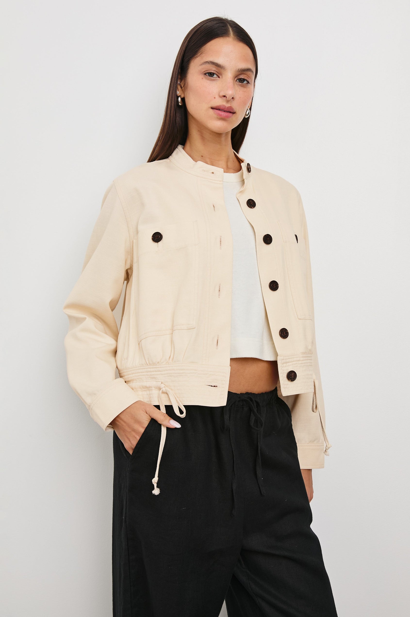 Alma Jacket with Button Closure, Mandarin Collar, Two Large Chest Button Patch Pockets and a Drawcord at the Hem in Ecru Colorway, with Dark Buttons - Front View Featured on Model
