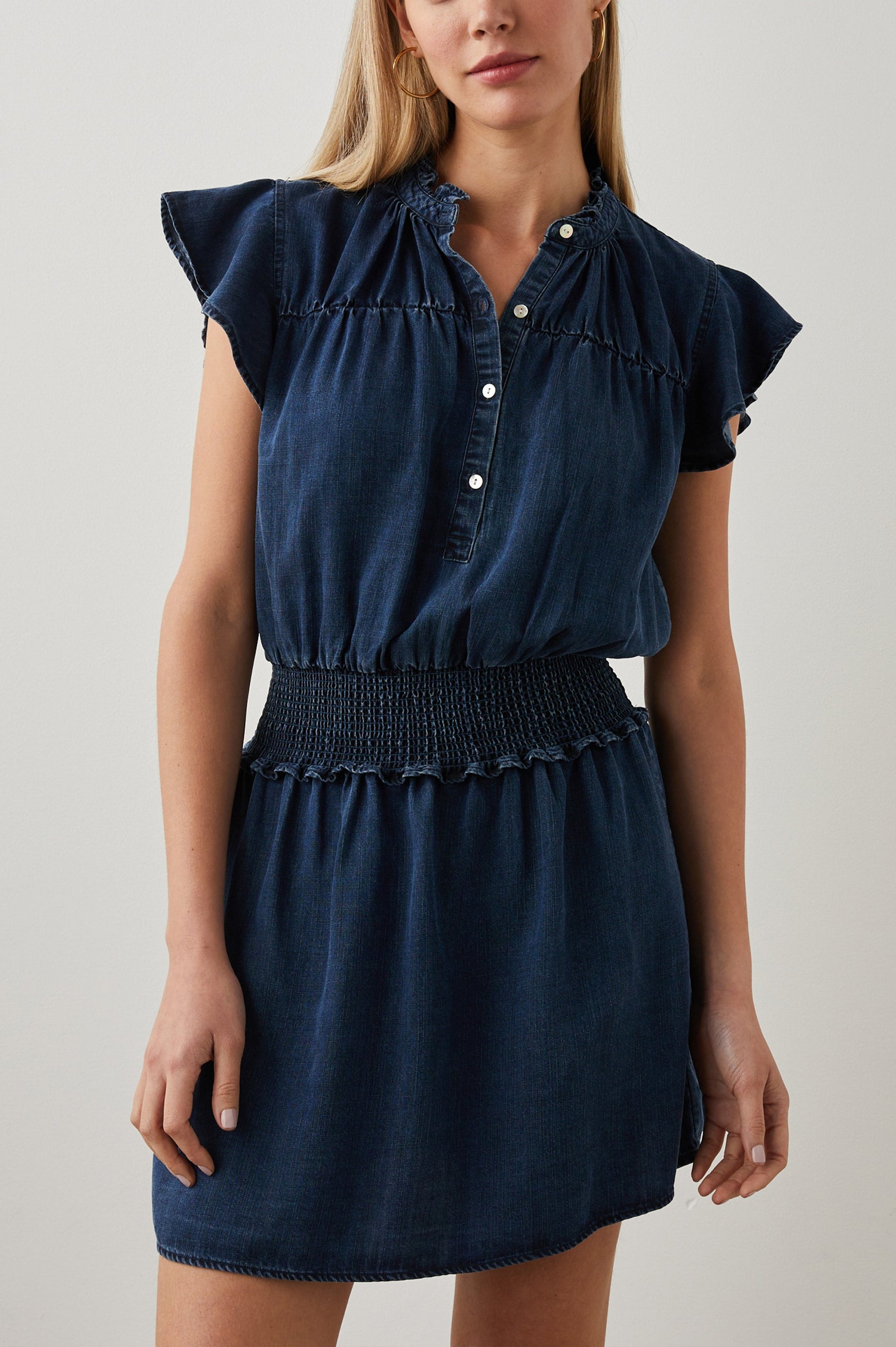 Amina Short Sleeve Denim Mini Dress with Flutter Sleeves, a Ruffled Collar, a Button Placket, and a Shirred Waist in Dark Vintage Colorway - Front View Featured on Model