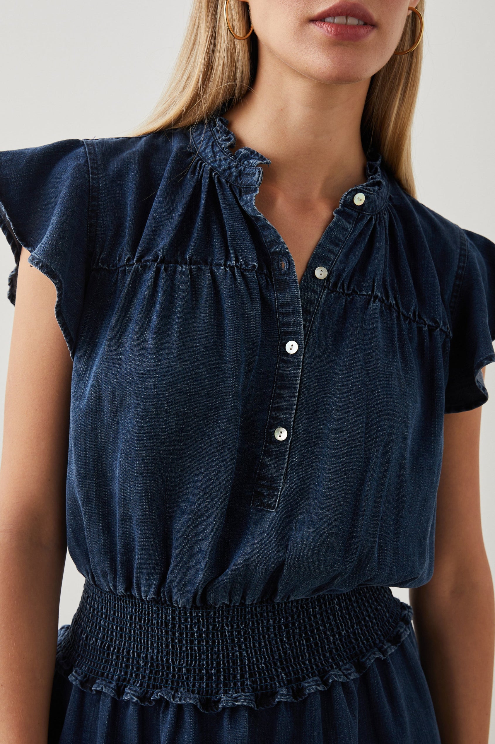 Amina Short Sleeve Denim Mini Dress with Flutter Sleeves, a Ruffled Collar, a Button Placket, and a Shirred Waist in Dark Vintage Colorway - Front View Featured on Model