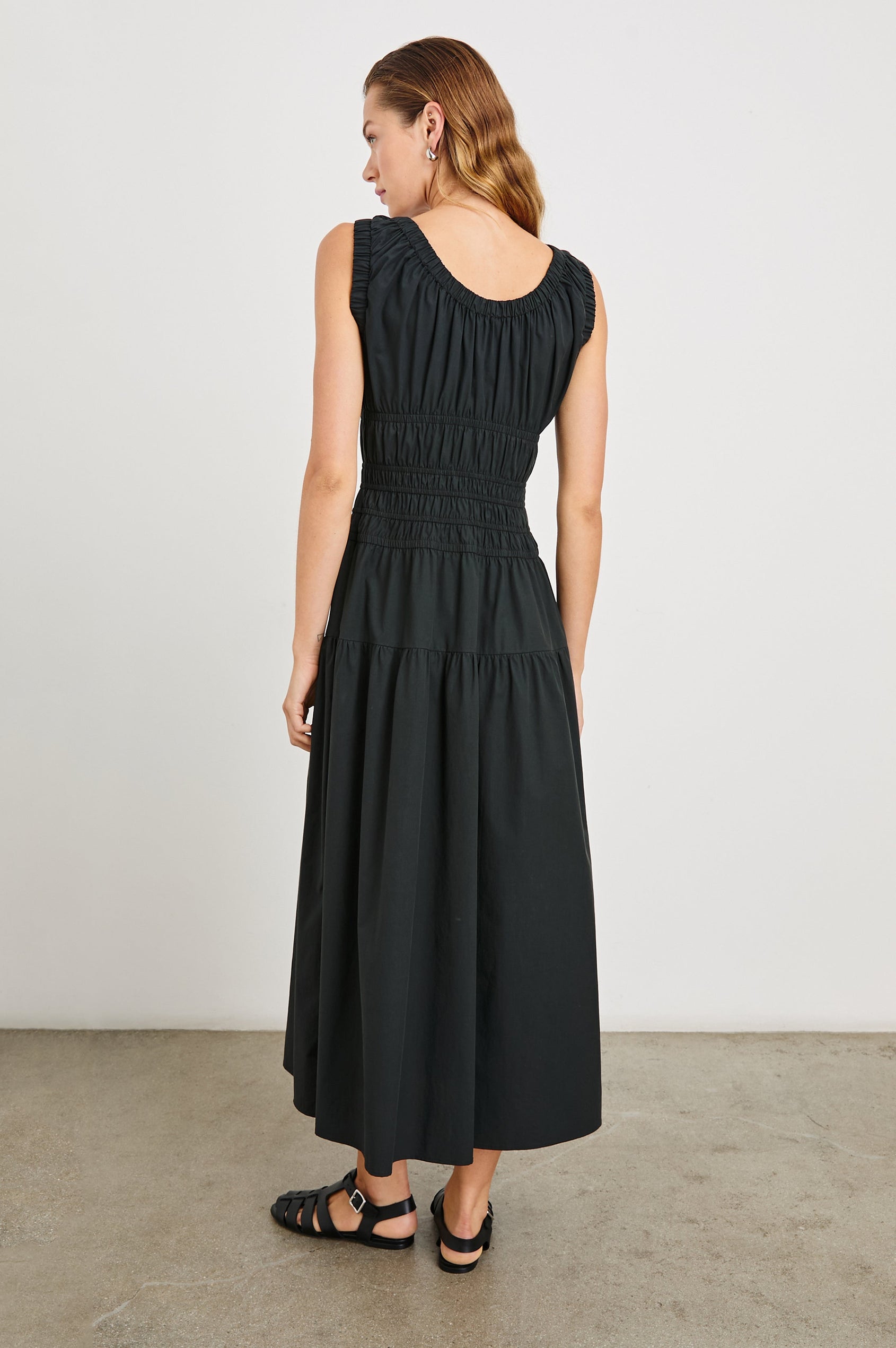 Anastasia Sleeveless Tiered Midi Dress with Shoulder Straps, a Scoop Neck and Ruching on the Bodice in Black Colorway - Back Full Body View Featured on Model