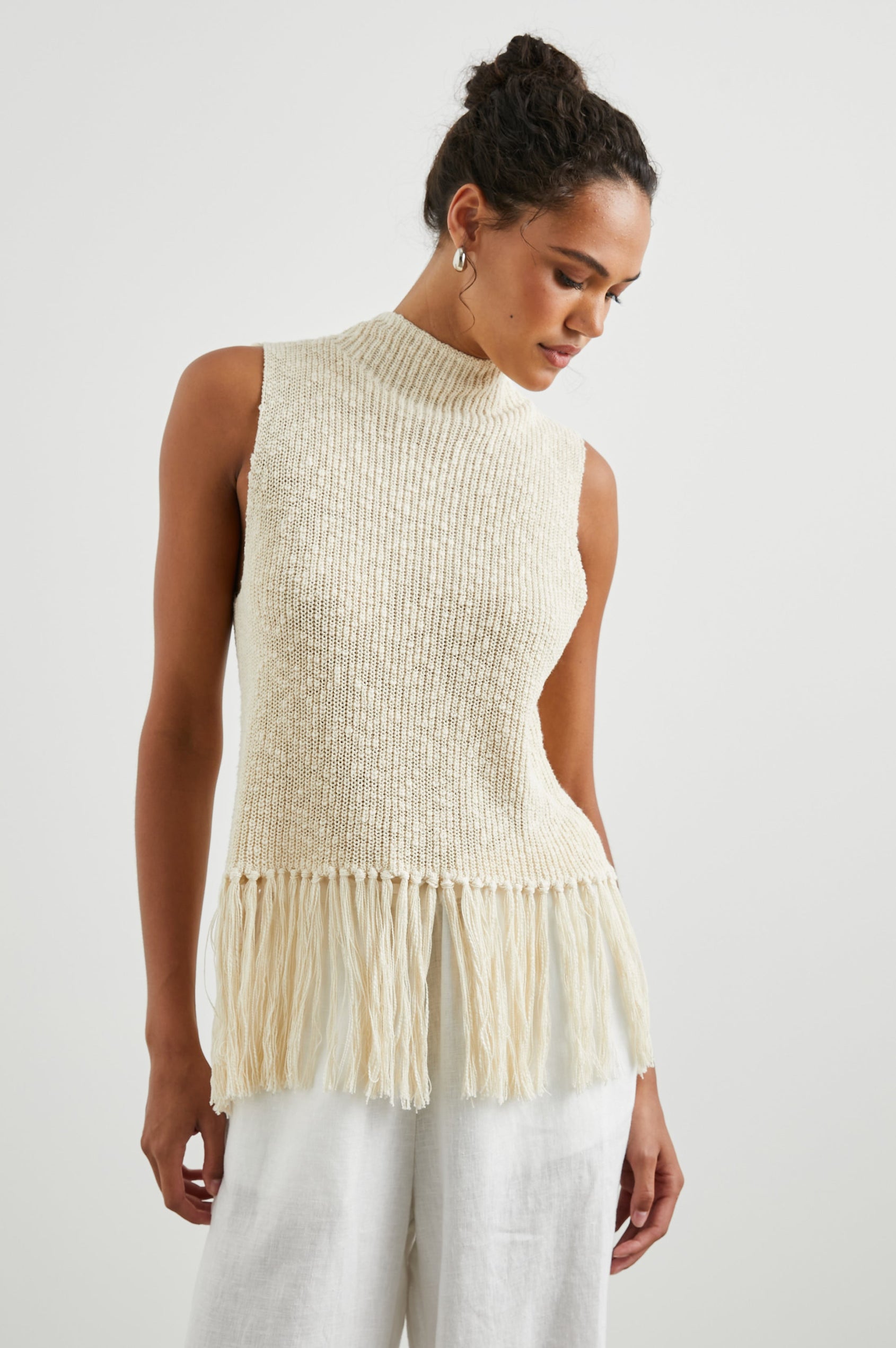 Astrid Sleeveless Knit Top with a Mock Neck, Fringe at the Hem, and Wide Arm Openings in Ecru Colorway - Front View Featured on Model