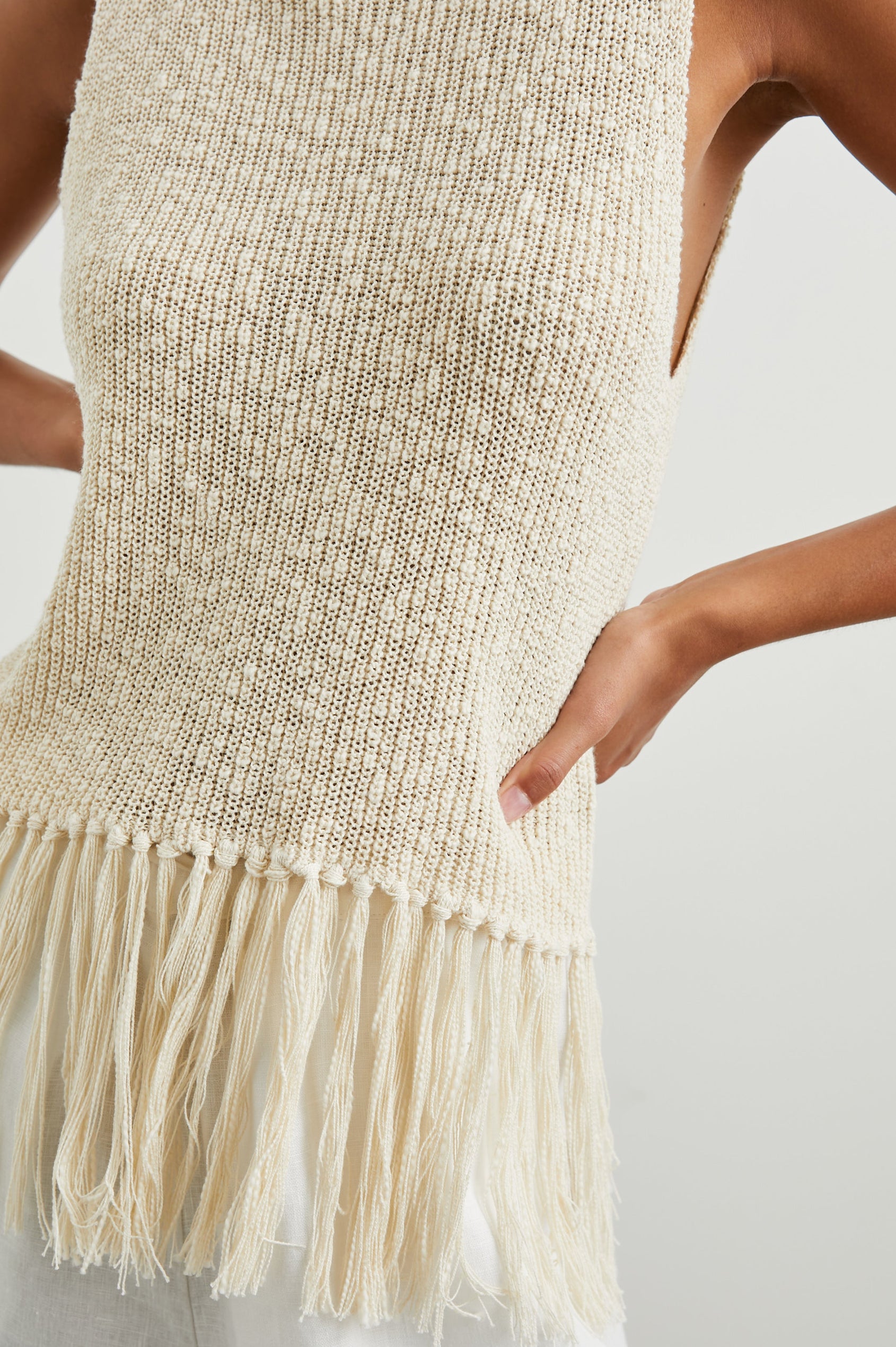 Astrid Sleeveless Knit Top with a Mock Neck, Fringe at the Hem, and Wide Arm Openings in Ecru Colorway - Front View Featured on Model