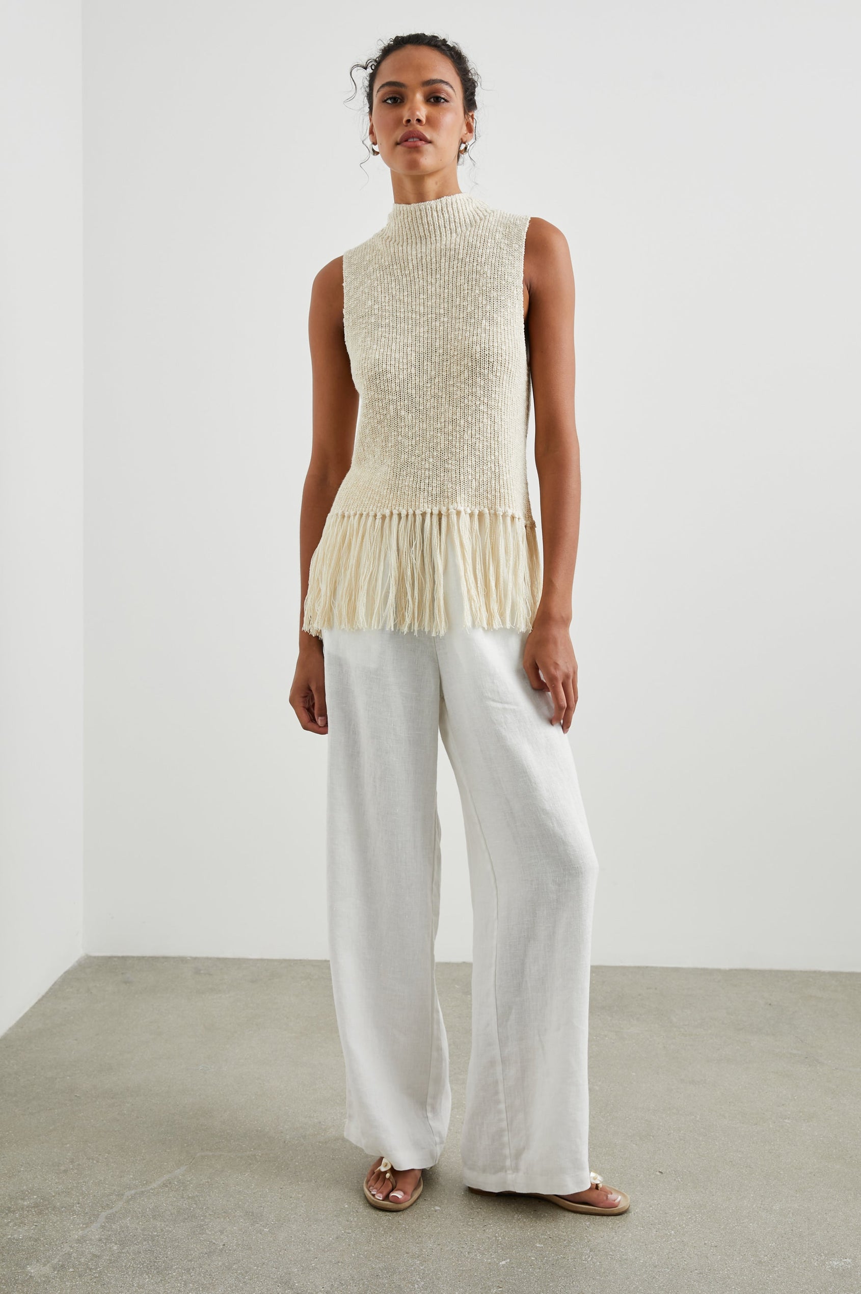 Astrid Sleeveless Knit Top with a Mock Neck, Fringe at the Hem, and Wide Arm Openings in Ecru Colorway - Front Full Body View Featured on Model