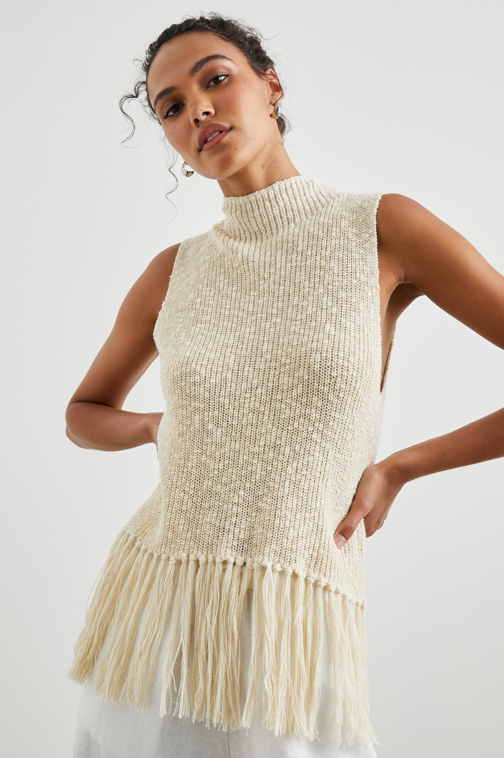 Astrid Sleeveless Knit Top with a Mock Neck, Fringe at the Hem, and Wide Arm Openings in Ecru Colorway - Front View Featured on Model