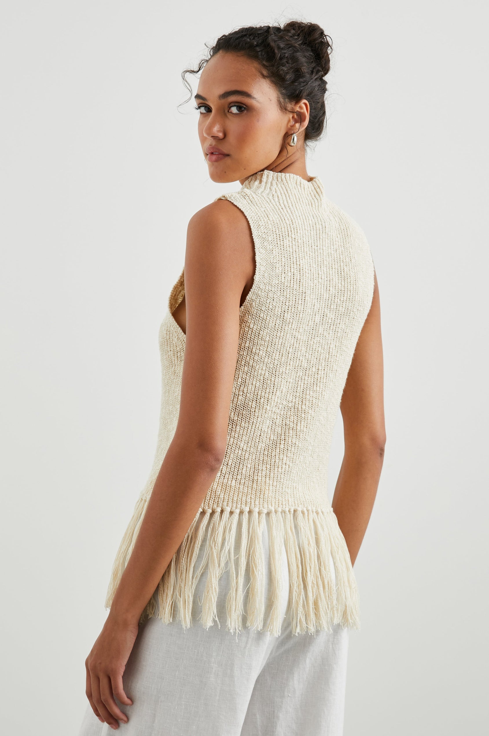 Astrid Sleeveless Knit Top with a Mock Neck, Fringe at the Hem, and Wide Arm Openings in Ecru Colorway - Back View Featured on Model