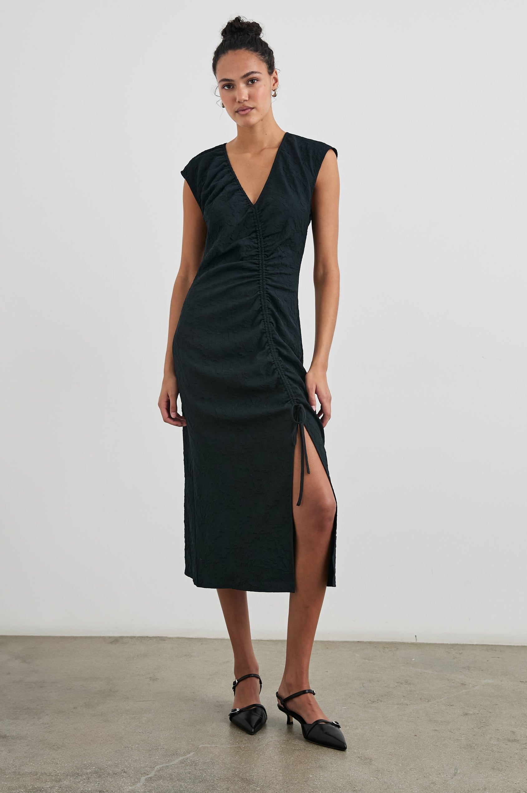 Auren Midi Dress with Cap Sleeves, a Deep V Neck, a Mid-Thigh Side Slit and Ruching from the V Neck to the Slit with a Drawcord at the Slit in Black Jacquard Colorway - Front Full Body View Featured on Model