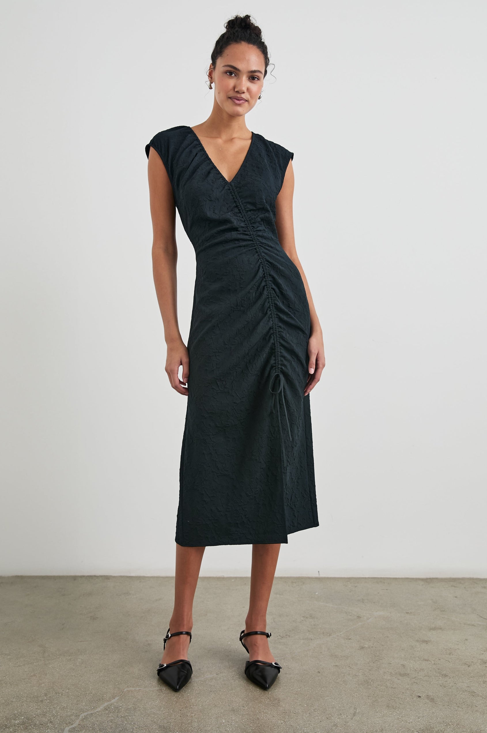 Auren Midi Dress with Cap Sleeves, a Deep V Neck, a Mid-Thigh Side Slit and Ruching from the V Neck to the Slit with a Drawcord at the Slit in Black Jacquard Colorway - Front Full Body View Featured on Model