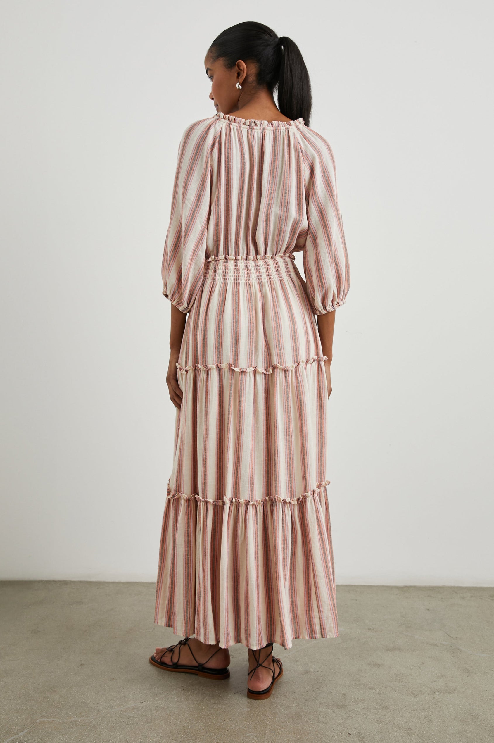 Caterine Maxi Dress with Mid-length Sleeves, a V neck, a Shirred Collar with a tie, a Smocked Waist, and a Tiered Skirt in Camino Stripe Colorway, a vertical stripe with cream, grey, purple and orange - Back Full Body View Featured on Model
