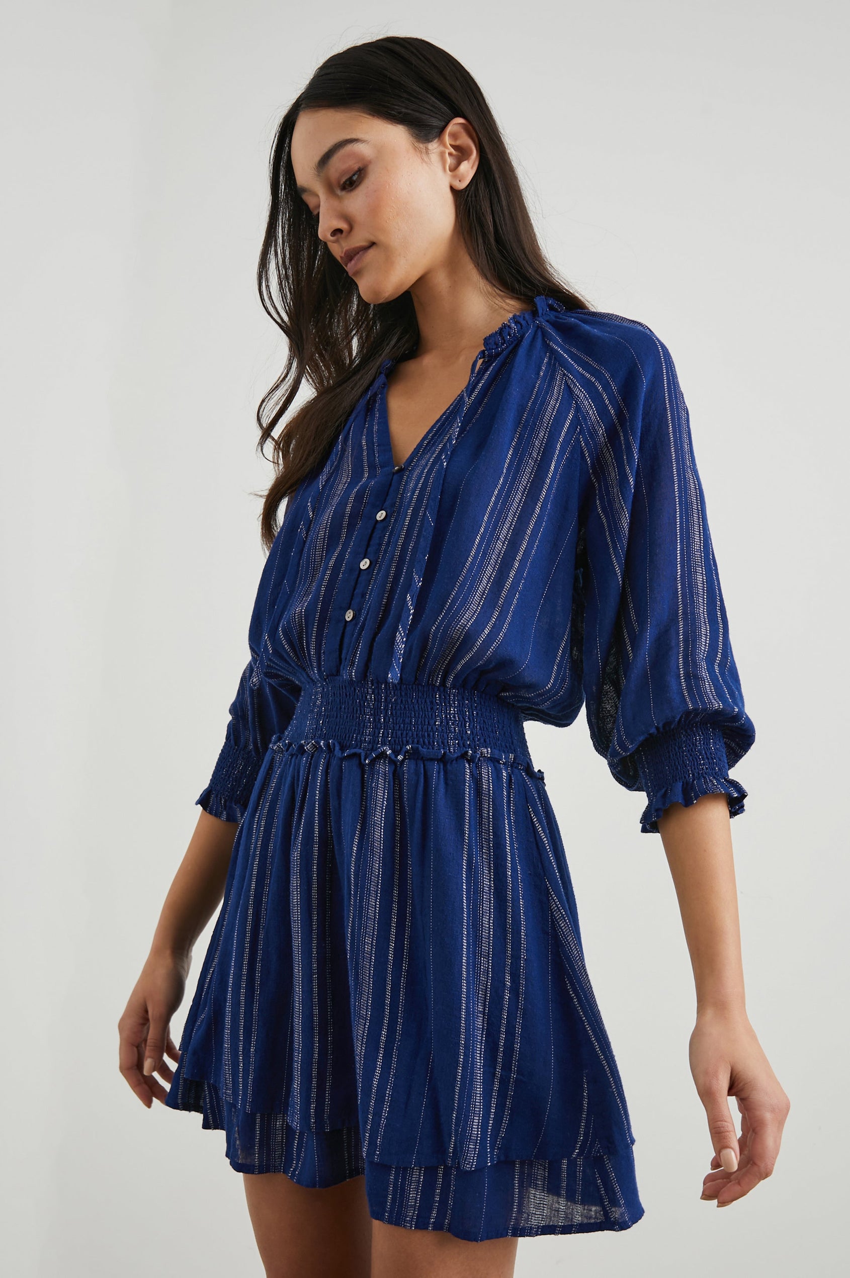 Crystal Mini Dress with Mid-Length Sleeves, Shirred Cuffs and Waist, a V Neck, Ties at the Collar, and Buttons down the Bodice in Noja Stripe Colorway, Thin White Vertical Stripes on Blue - Front View Featured on Model