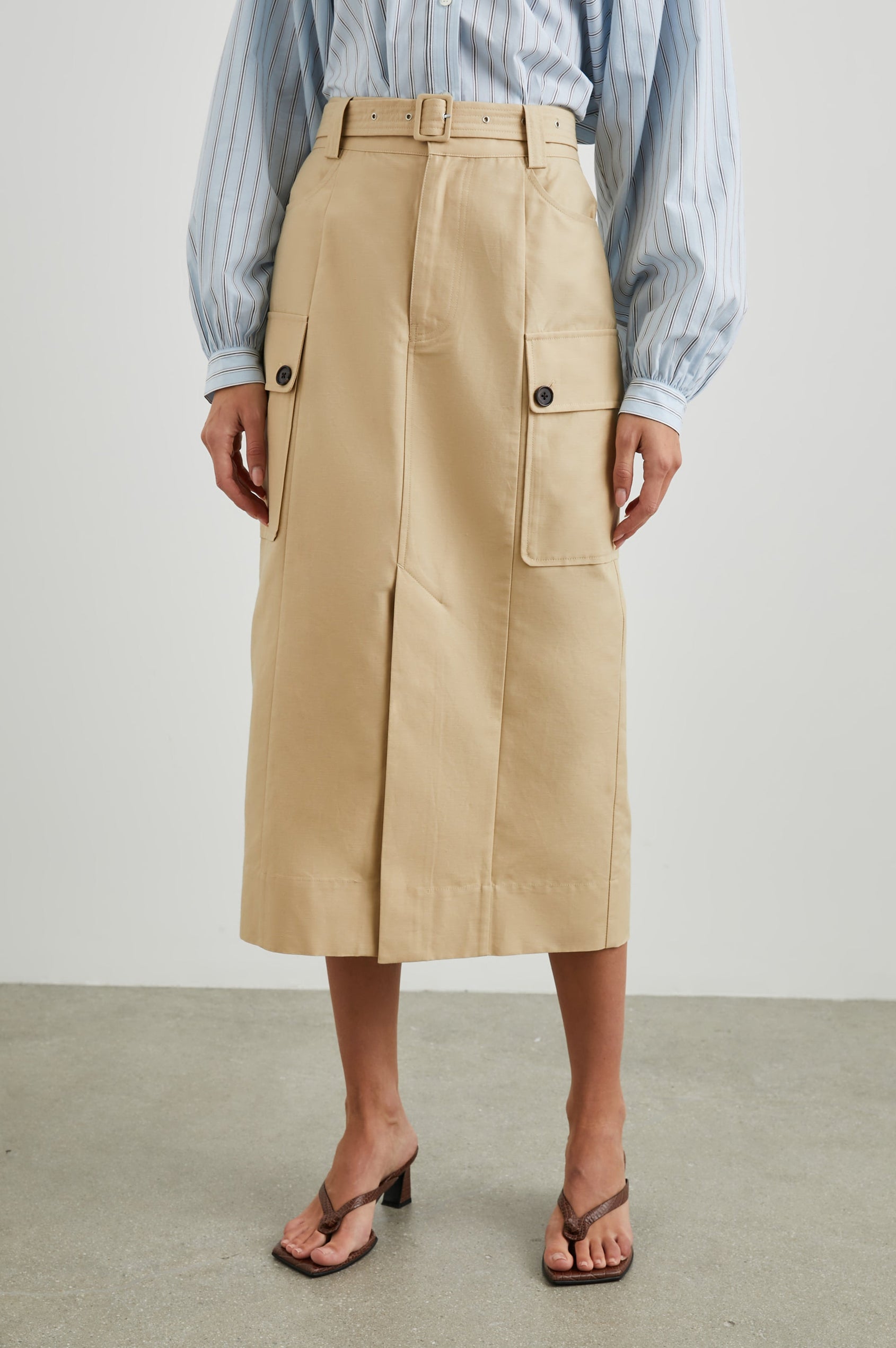 Cyrus Midi Skirt with a Center Slit, Belt Loops, a Fabric Belt, Two Front Pockets and Two Side Button Flap Pockets in Khaki Colorway, with Dark Buttons - Front View Featured on Model