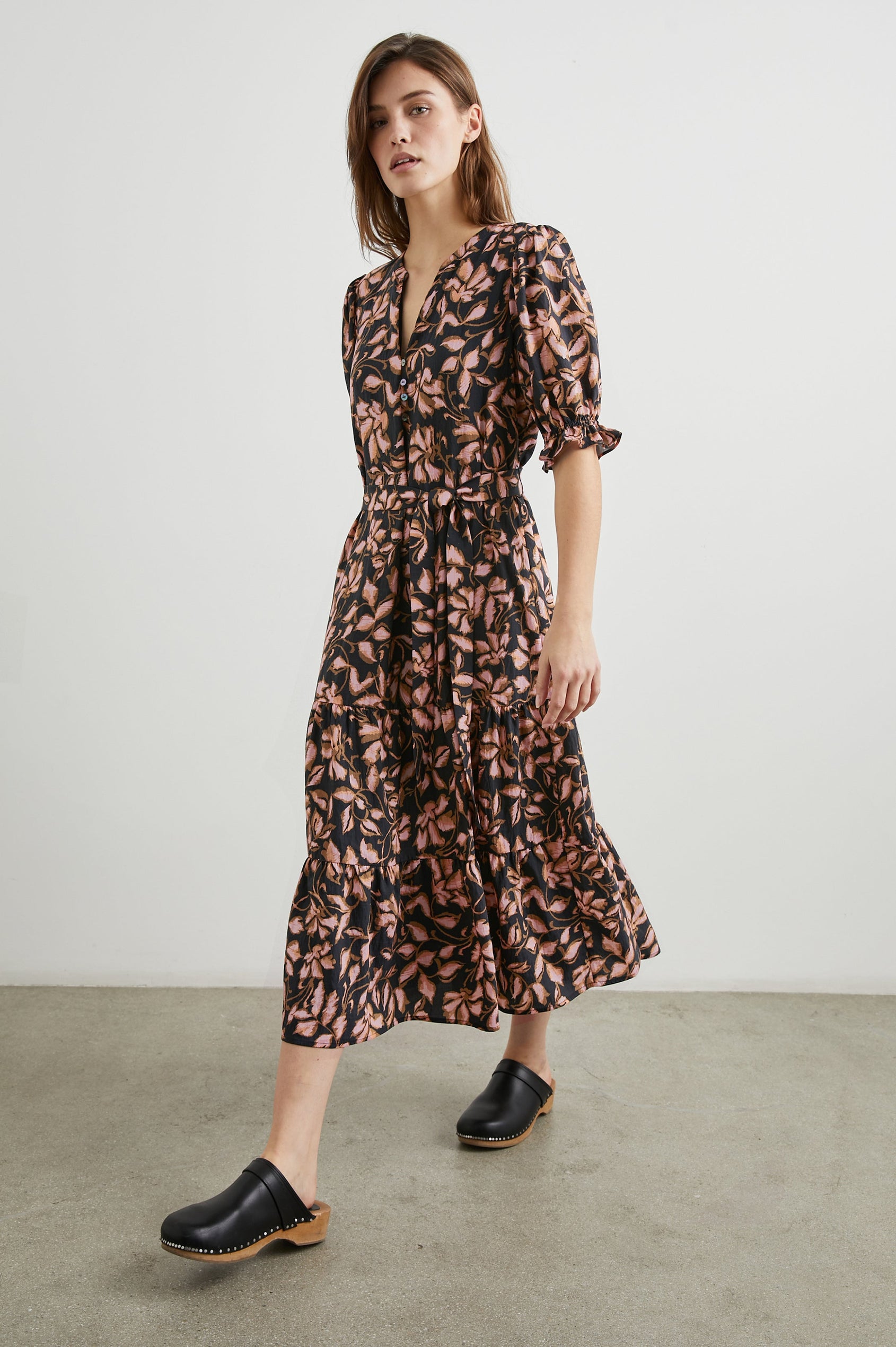 Eliana Midi Dress with Elbow-Length Sleeves with Shirred Cuffs, a V Neck, Buttons Down the Bodice, a Fabric Tie at the Waist  and a Tiered Skirt in Jasmine Colorway, a Floral Pattern in Pink and Brown on Black - Front Full Body View Featured on Model