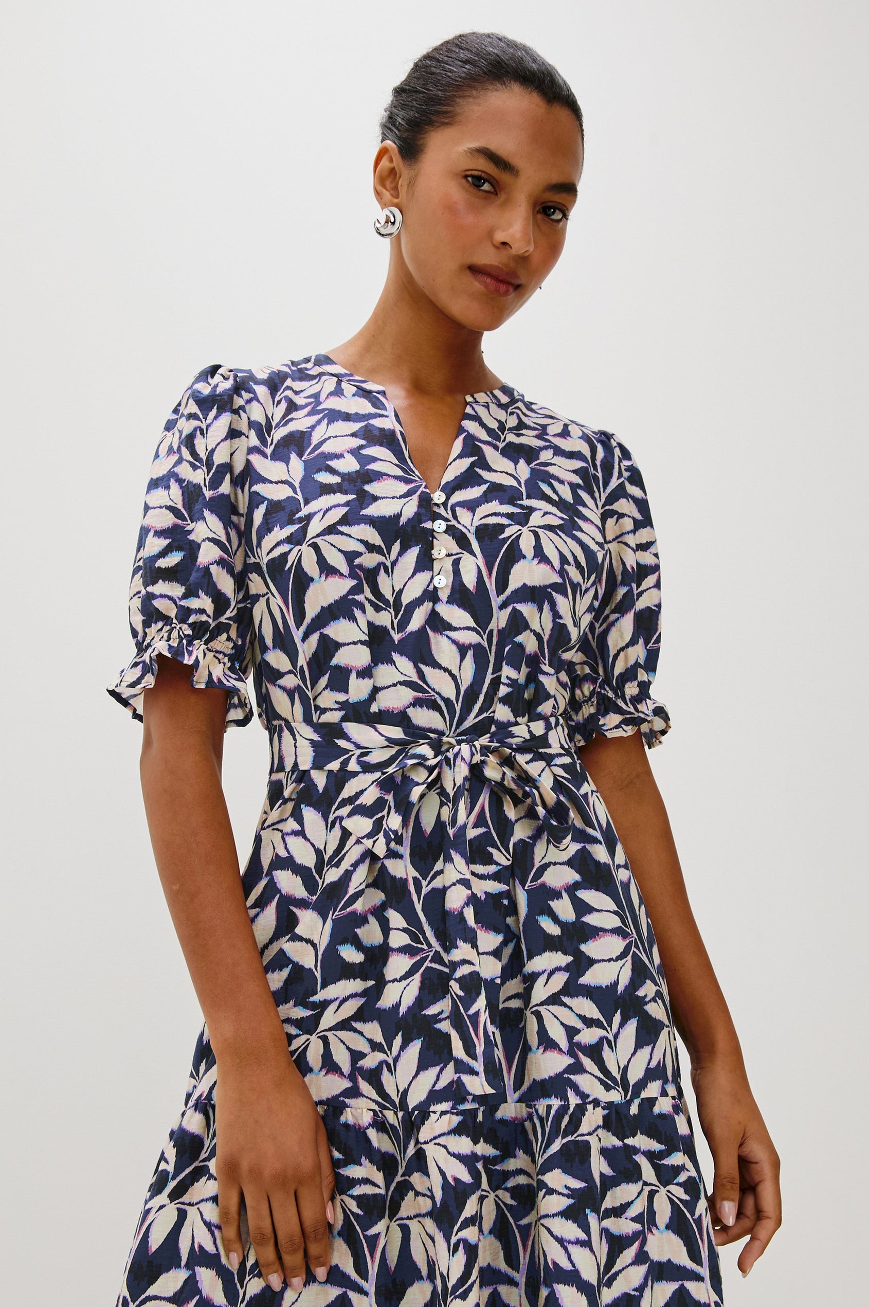 Eliana Midi Dress with Elbow Length Sleeves with Elasticated Ruffle Hem, V-Neck, 3-Button Front, Self Waist Tie and Tiered Skirt in Navy Vines Colorway. Front View Featured on Model.