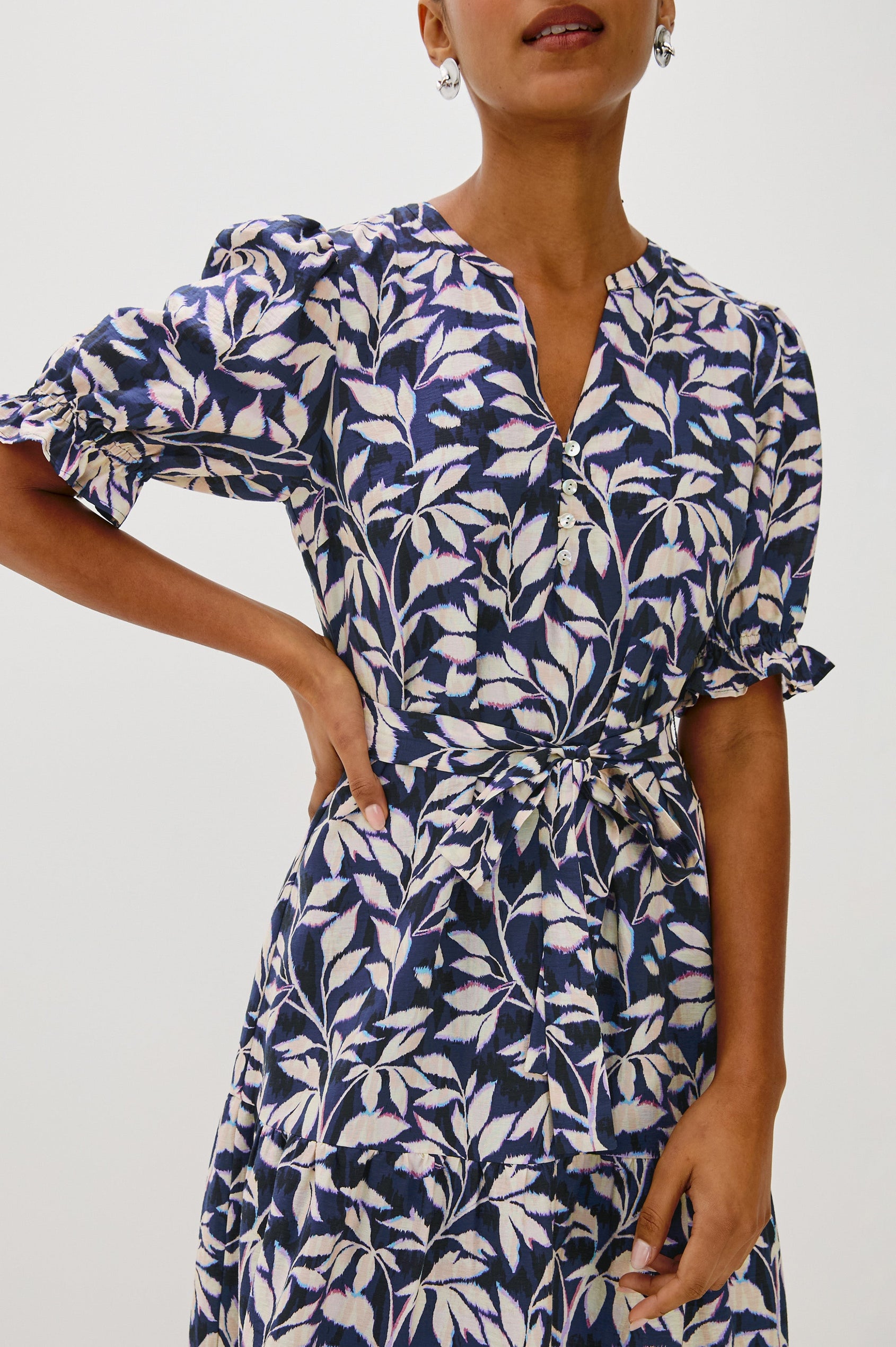 Eliana Midi Dress with Elbow Length Sleeves with Elasticated Ruffle Hem, V-Neck, 3-Button Front, Self Waist Tie and Tiered Skirt in Navy Vines Colorway. Front Detail View Featured on Model.