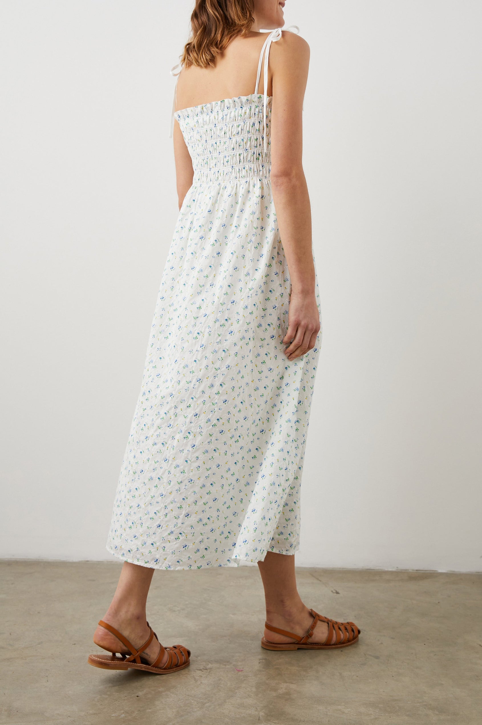 Faith Sleeveless Midi Dress with a Square Neckline, Tie Spaghetti Straps, Eyelets Across the Dress, and a Smocked Bodice in Bluebell Eyelet Colorway, Small Blue, Yellow and Green Flowers on White - Back Full Body View Featured on Model