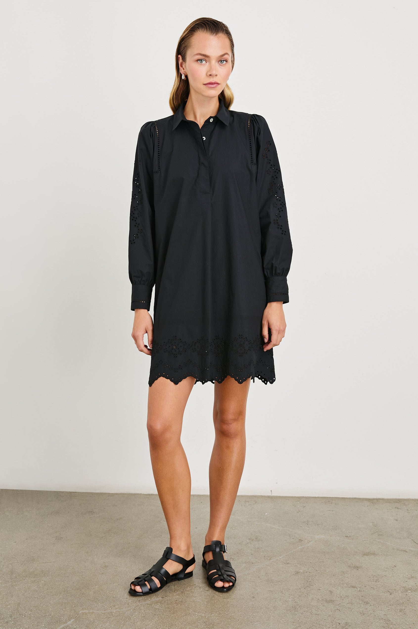 Fernanda Long-Sleeve Mini Dress with Button Cuffs, a Collar, a Placket with Buttons, a Scalloped Hem, a Floral Eyelet Design on the Sleeves and a Floral and Geometric Eyelet Design on the Hem in Black Eyelet Colorway - Front Full Body View Featured on Model