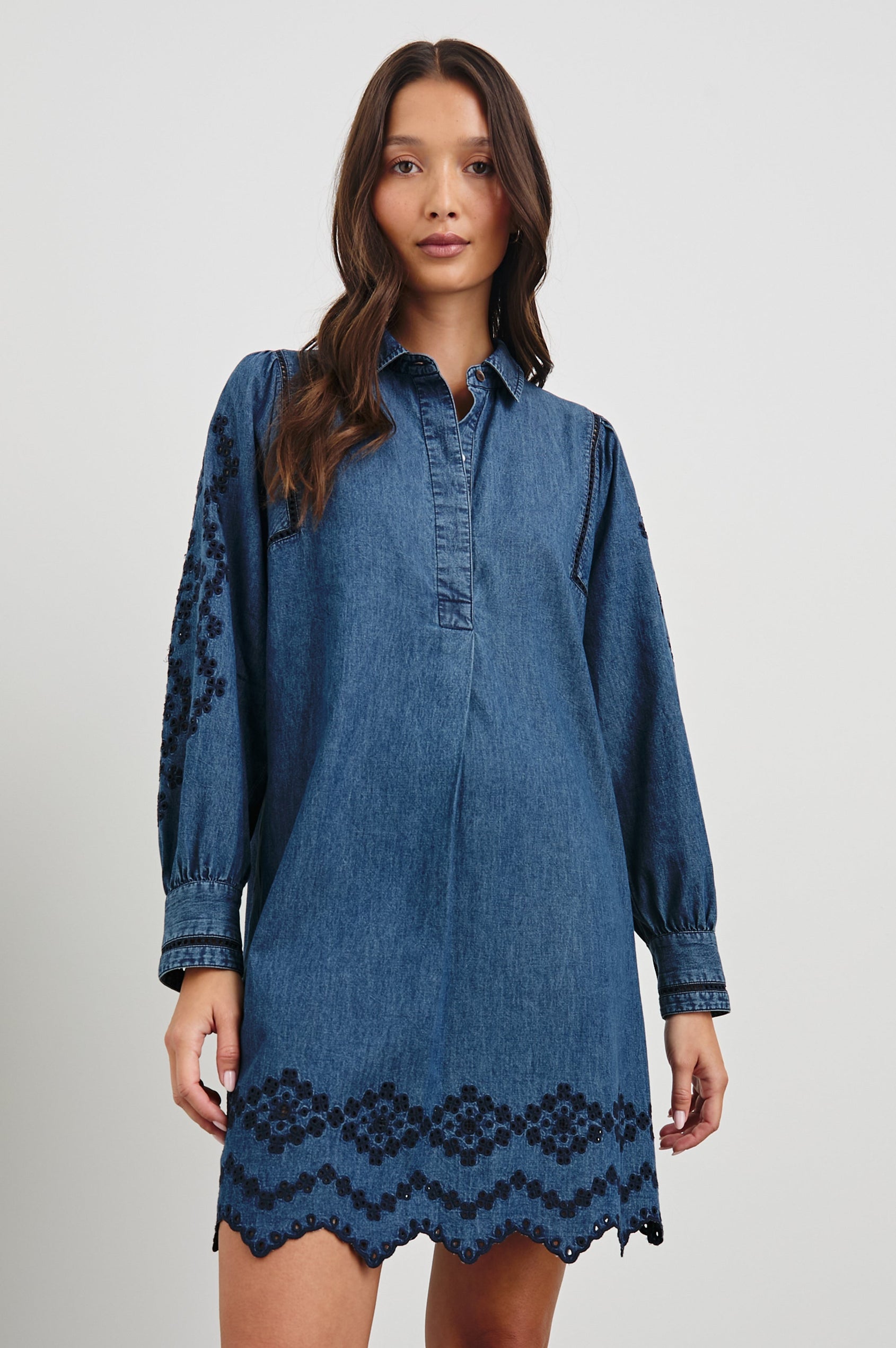 Fernanda Long-Sleeve Mini Dress with Button Cuffs, a Collar, a Placket with Buttons, a Scalloped Hem, a Floral Eyelet Design on the Sleeves and a Floral and Geometric Eyelet Design on the Hem in Dark Vintage Wash Colorway - Front View Featured on Model
