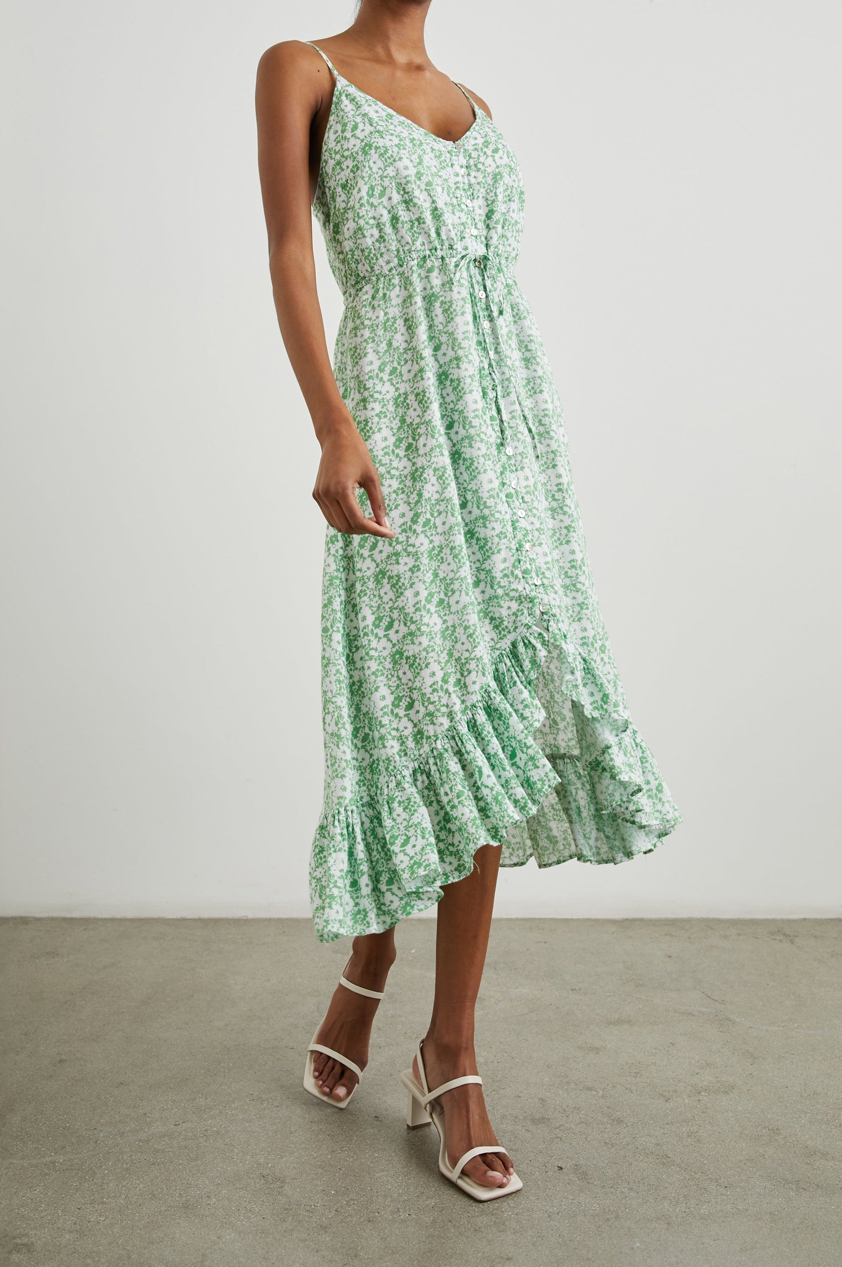 Frida Midi Dress with a Deep V Neck, Adjustable Spaghetti Straps, a Ruffled Hem, Drawstring Waist Ties and Buttons Down the Front in Green Texture Floral Colorway, Green and White Flowers - Side Full Body View Featured on Model