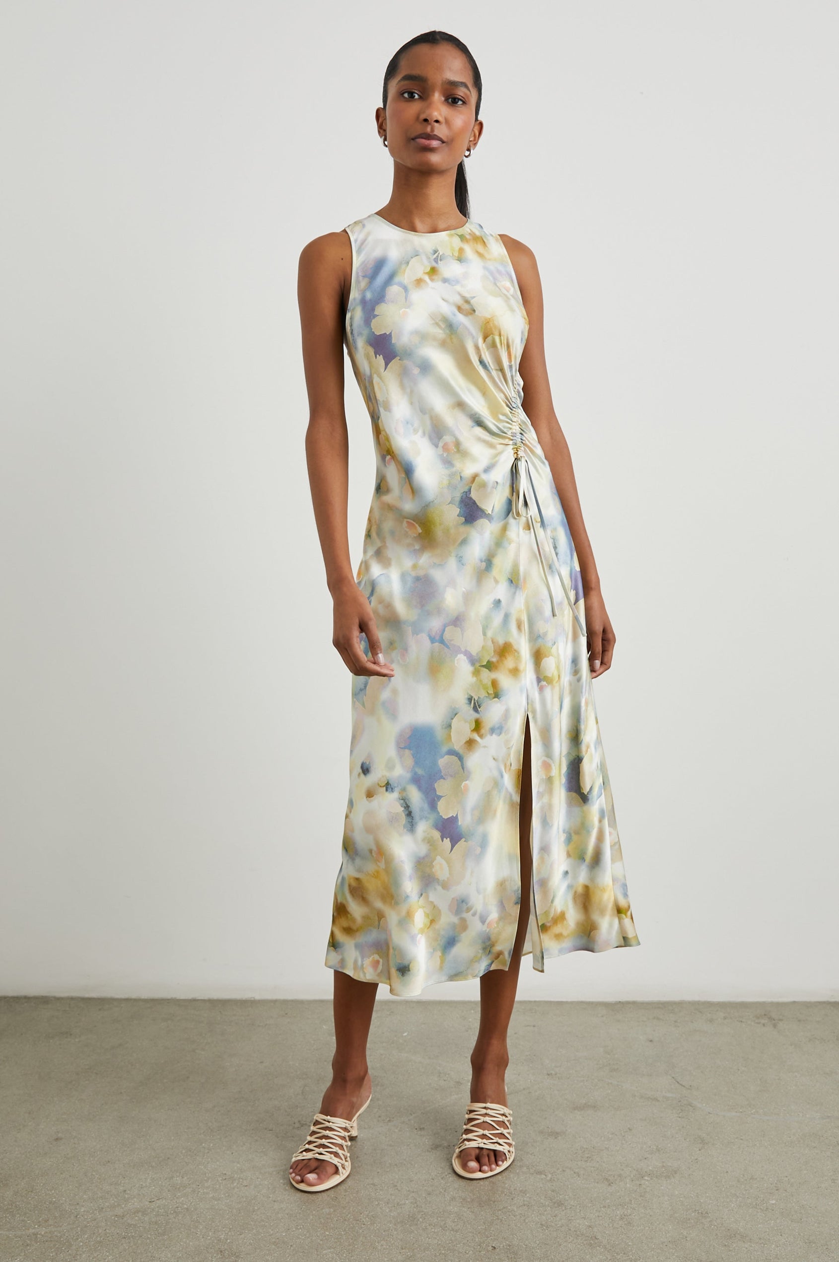 Gabriella Sleeveless Midi Dress with a Crew Neck, a Left Thigh Side Slit, a Ruched Drawstring on the Left Side and a Keyhole Button Closure at the Back in Diffused Blossom Colorway, Flowers in Golds, Creams and Blues on White - Front Full Body View Featured on Model