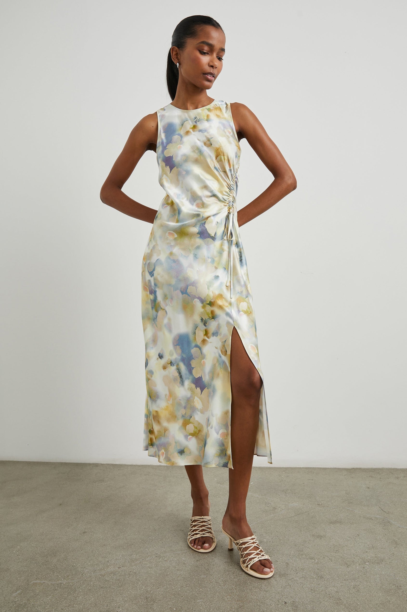 Gabriella Sleeveless Midi Dress with a Crew Neck, a Left Thigh Side Slit, a Ruched Drawstring on the Left Side and a Keyhole Button Closure at the Back in Diffused Blossom Colorway, Flowers in Golds, Creams and Blues on White - Front Full Body View Featured on Model