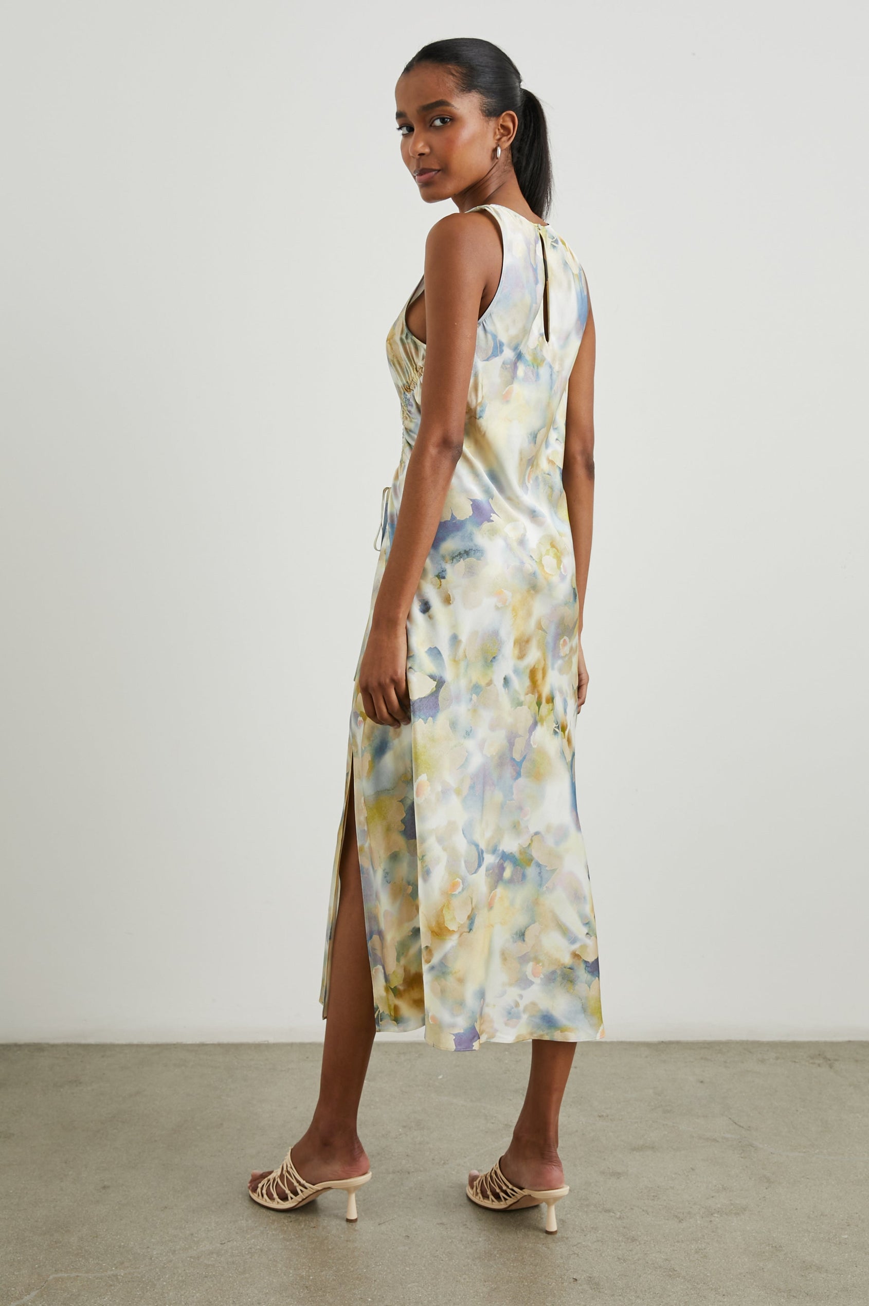 Gabriella Sleeveless Midi Dress with a Crew Neck, a Left Thigh Side Slit, a Ruched Drawstring on the Left Side and a Keyhole Button Closure at the Back in Diffused Blossom Colorway, Flowers in Golds, Creams and Blues on White - Back Full Body View Featured on Model