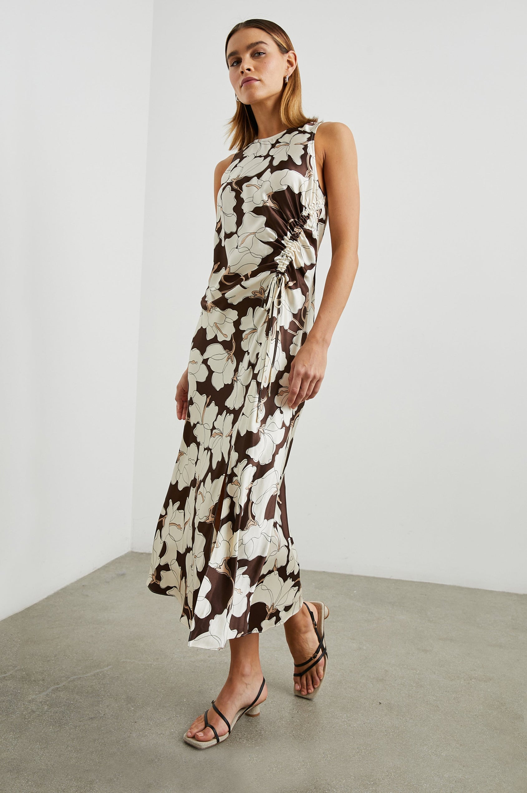 Gabriella Sleeveless Midi Dress with a Crew Neck, a Left Thigh Side Slit, a Ruched Drawstring on the Left Side and a Keyhole Button Closure at the Back in Mocha Floral Colorway, Flowers in Cream and Tan on Mocha - Front Full Body View Featured on Model