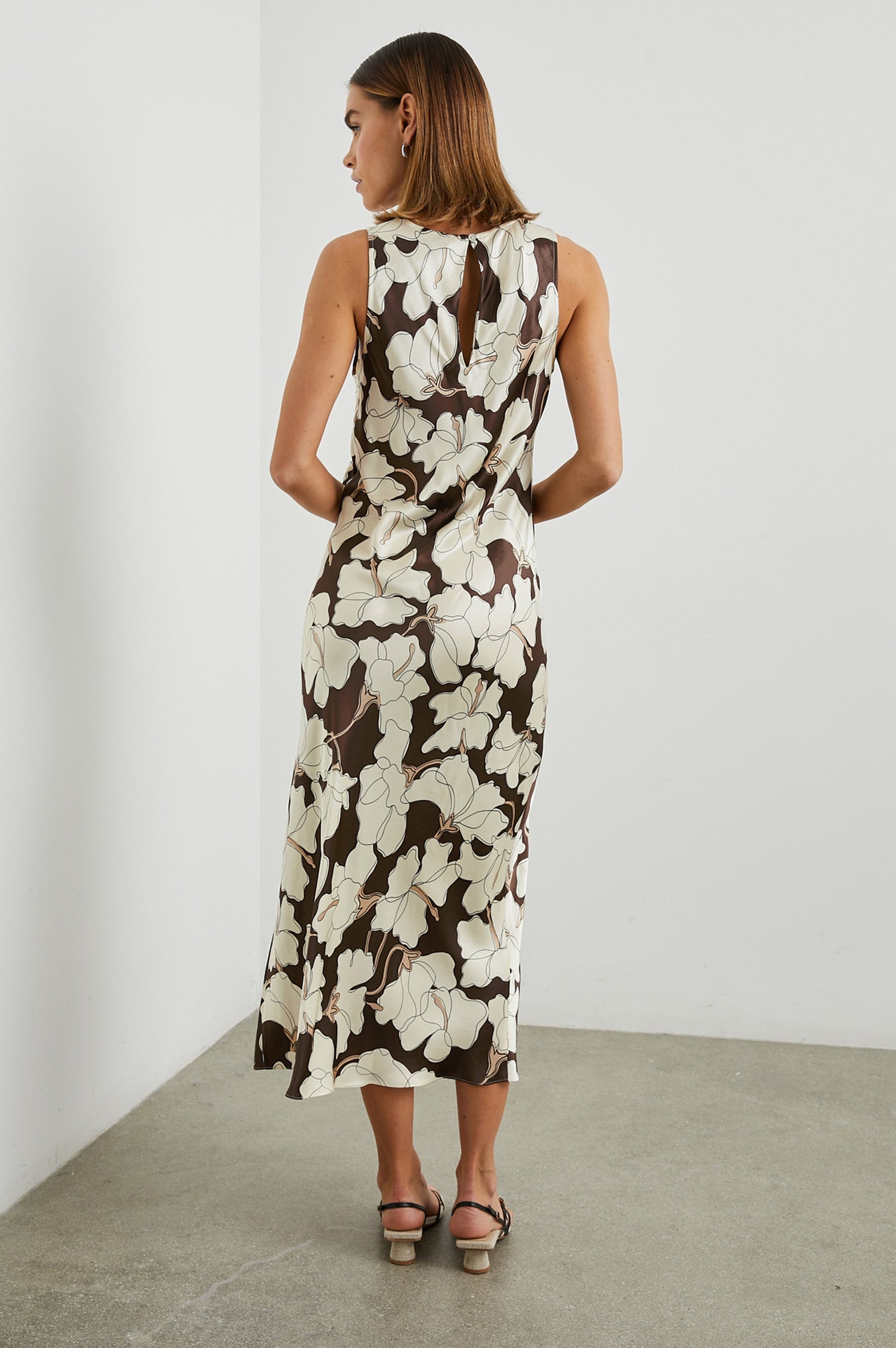 Gabriella Sleeveless Midi Dress with a Crew Neck, a Left Thigh Side Slit, a Ruched Drawstring on the Left Side and a Keyhole Button Closure at the Back in Mocha Floral Colorway, Flowers in Cream and Tan on Mocha - Back Full Body View Featured on Model