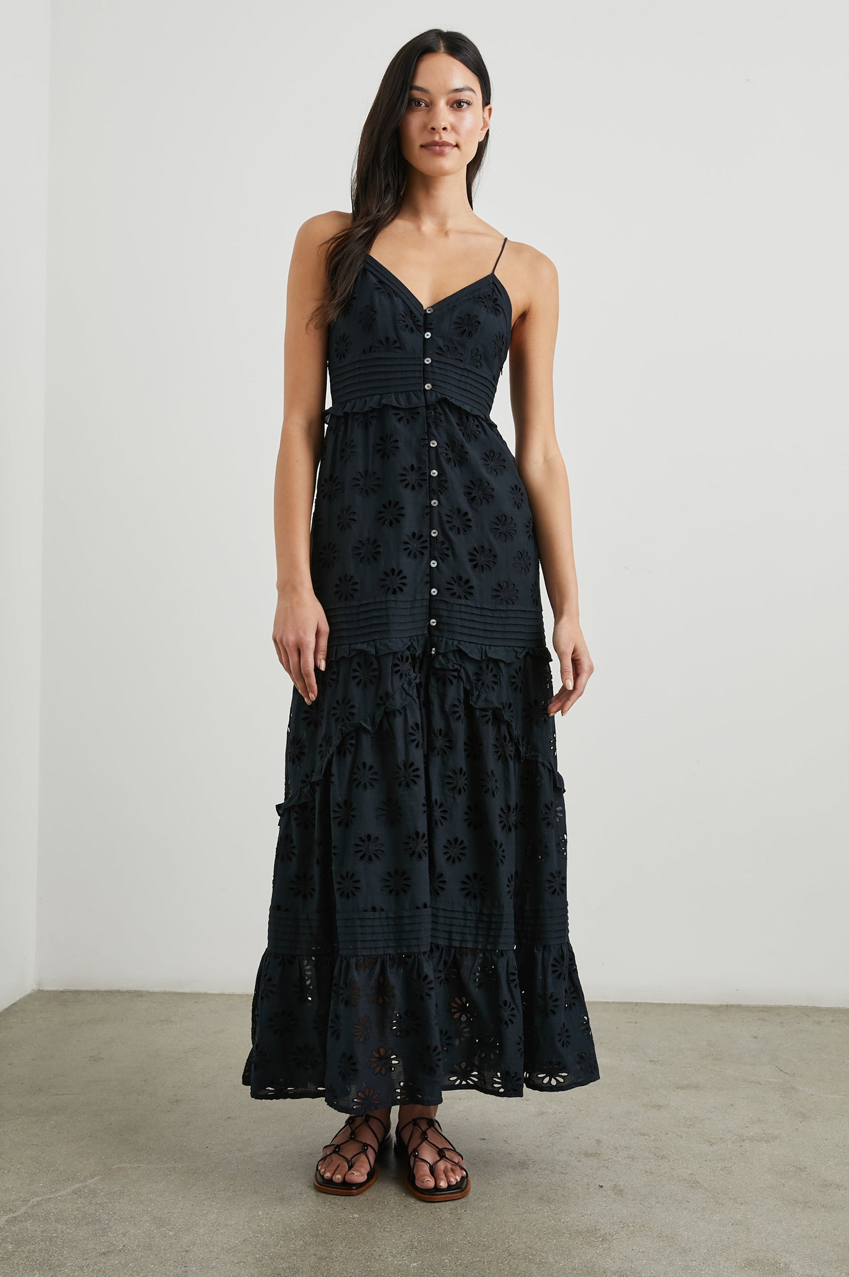 Henrietta Sleeveless Maxi Dress with Adjustable Spaghetti Straps, a Deep V Neck, Buttons Down the Front, a Shirred Back Bodice, a Tiered Skirt with Ruffles and Horizontal Pleats, and a Floral Eyelet Design in Black Colorway - Front Full Body View Featured on Model