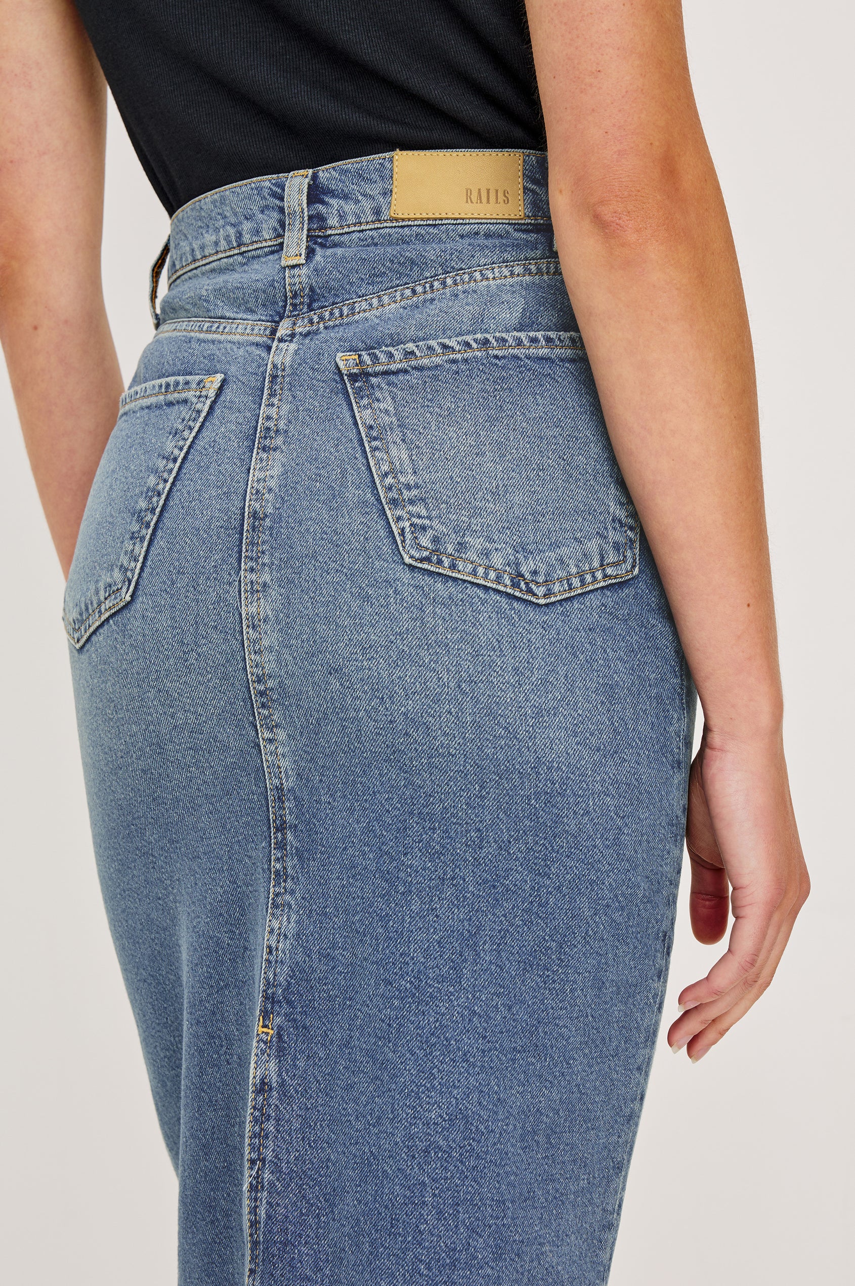 Highland Denim Midi Skirt with a Raw Hem, a Back Vent, Additional Front Seams, Belt Loops, Two Front Pockets plus a Coin Pocket and Two Back Patch Pockets in Vintage Sapphire Colorway - Back View Featured on Model