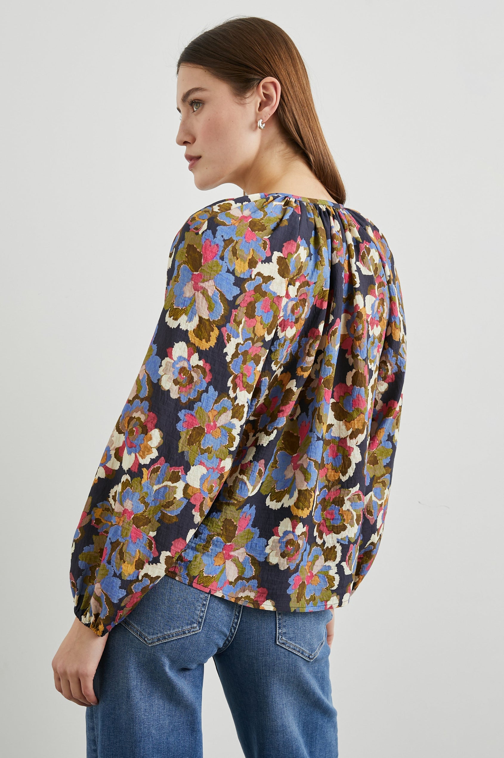 Indi Top with a V Neckline with a Button Placket, Pleating at Back Neckline and Elastic Cuffs in Navy Wildflower Colorway, with blue, gold, green and cream flowers on navy - Back untucked View Featured on Model