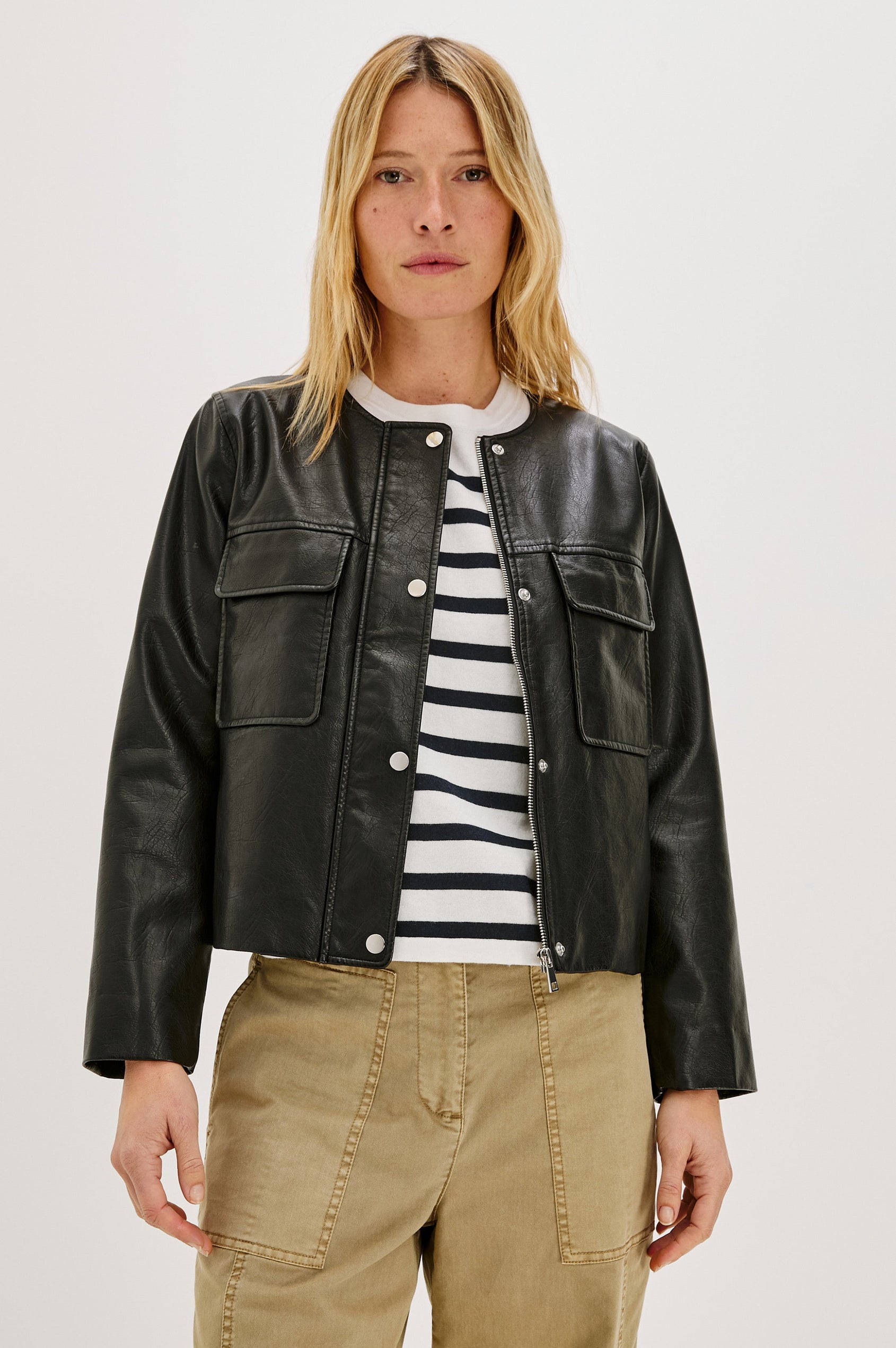 Inka, a cropped, boxy faux leather jacket in a black, slightly distressed finish. The design includes classic chest pockets and a structured silhouette. Front View featured on model, Unzipped