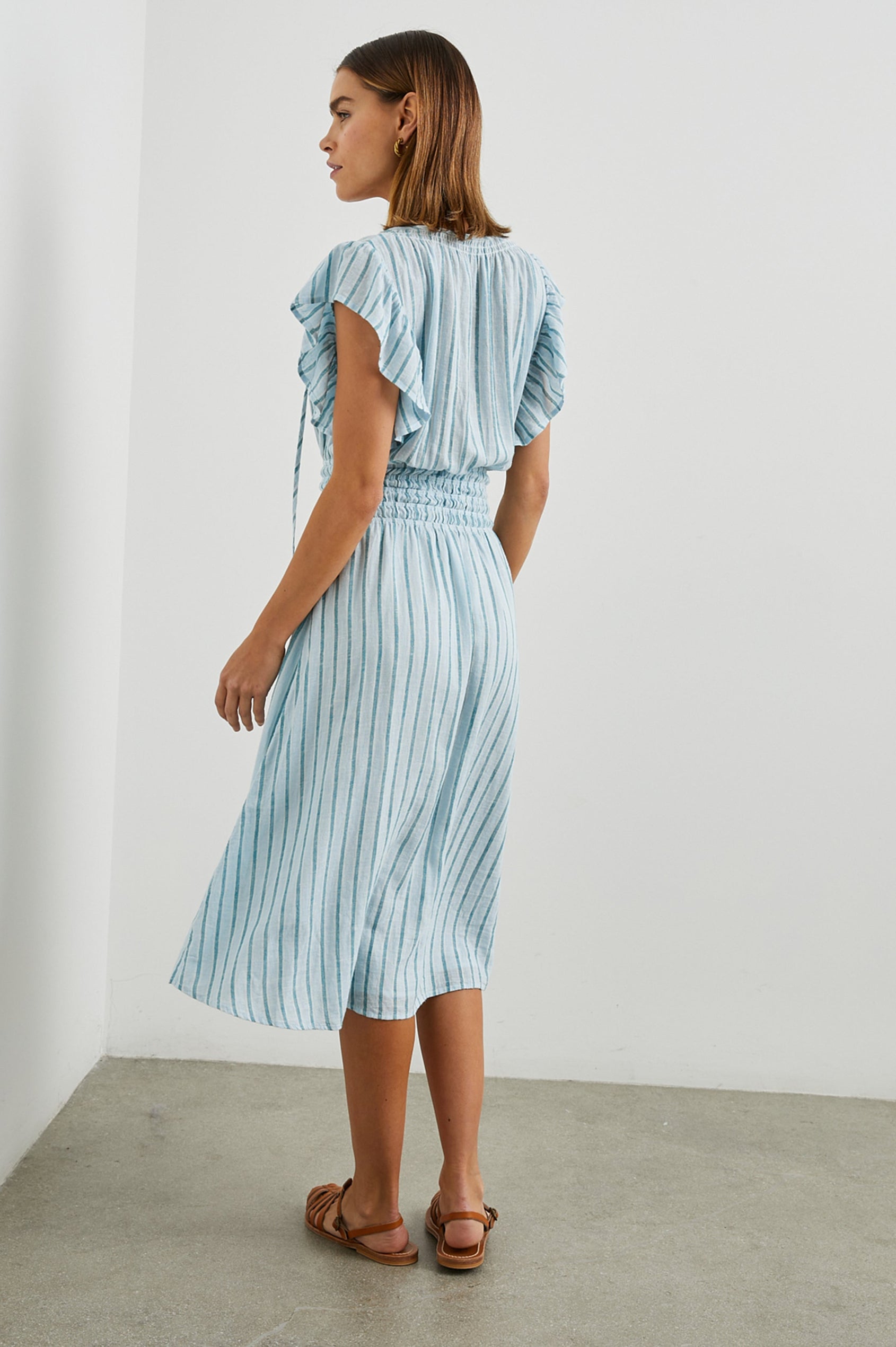Iona Short Sleeve Midi Dress with Flutter Sleeves, a Deep V Neck with Ties, and a Shirred Waist in Cambria Stripe Colorway, Vertical Stripes in White, Blue and Light Blue - Back Full Body View Featured on Model