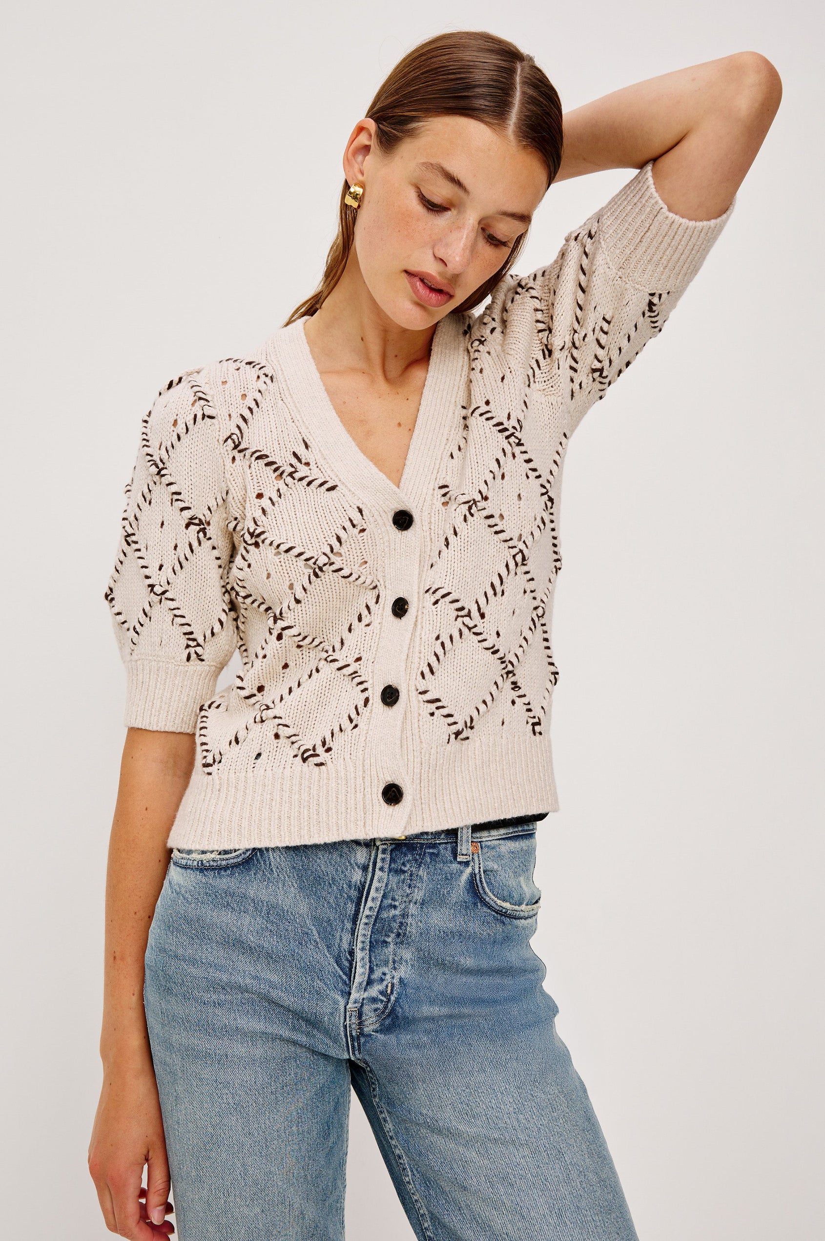 The Isla is a half sleeve cardigan, v-neck and button front with cross hatch rope applique and rib trim in Oat colorway. Front view featured on model.