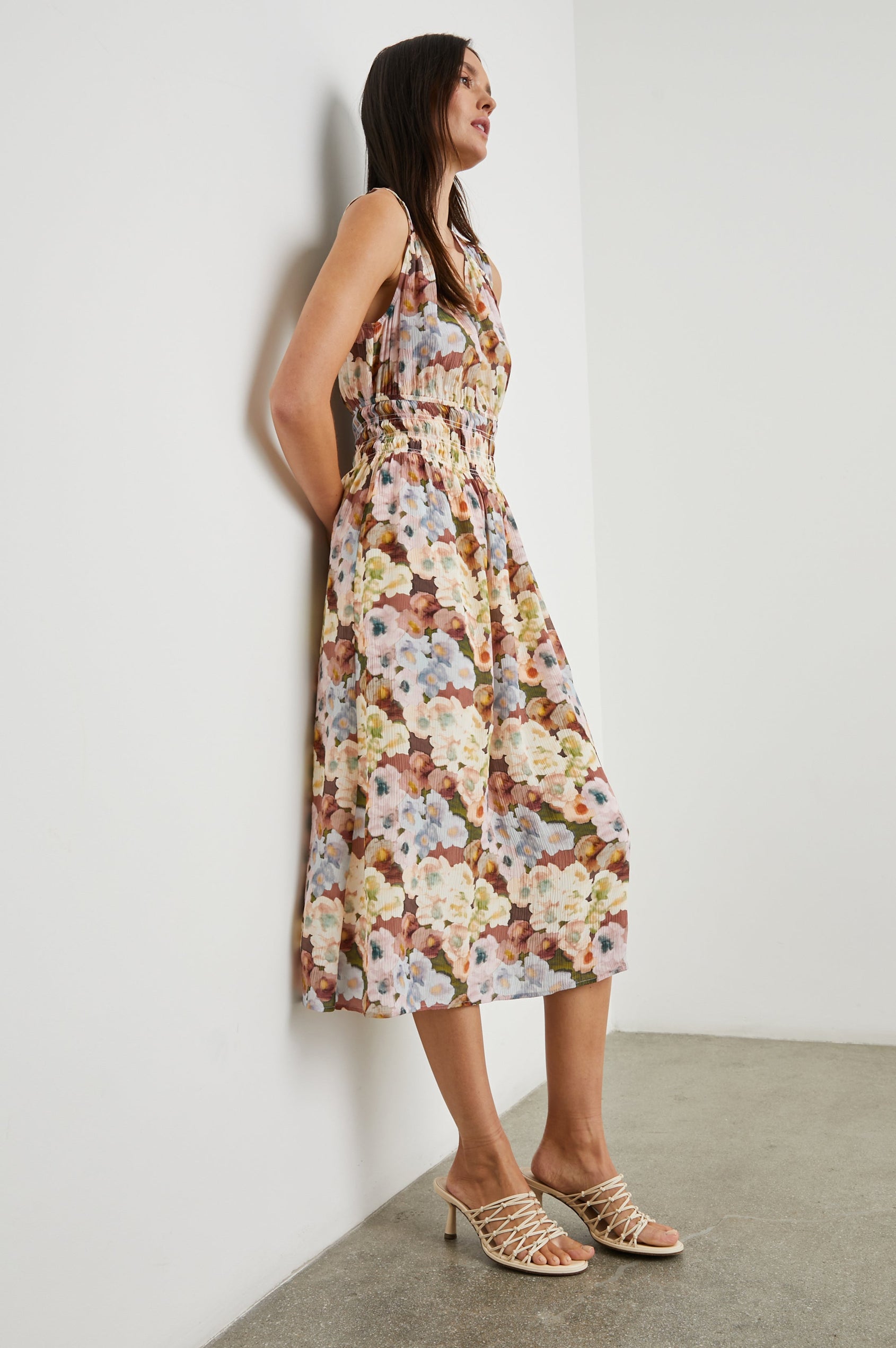 Izzy Sleeveless Midi Dress with Wide Smocked Shoulder Straps, a Smocked Waist and a Deep V Neck, in Painted Floral Colorway, in Browns, Yellows, Pinks, Blues and Greens - Side Full Body View Featured on Model