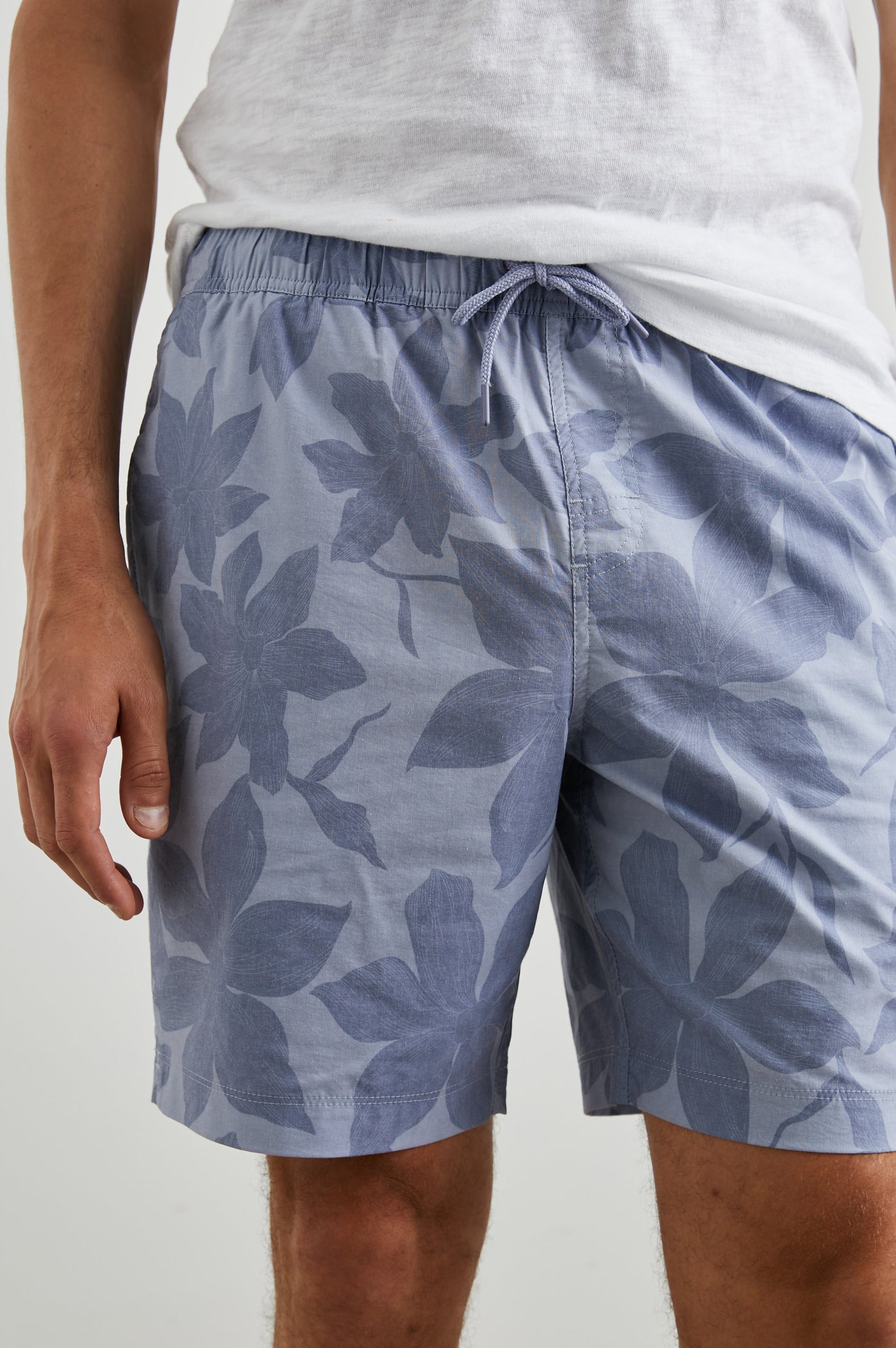 Kian Swim Shorts with an Elastic Drawstring Waistband, Two Front Pockets and a Back Button Flap Pocket in Garden Sands Orchid Colorway, Blue Orchids on Light Blue - Front View Featured on Model