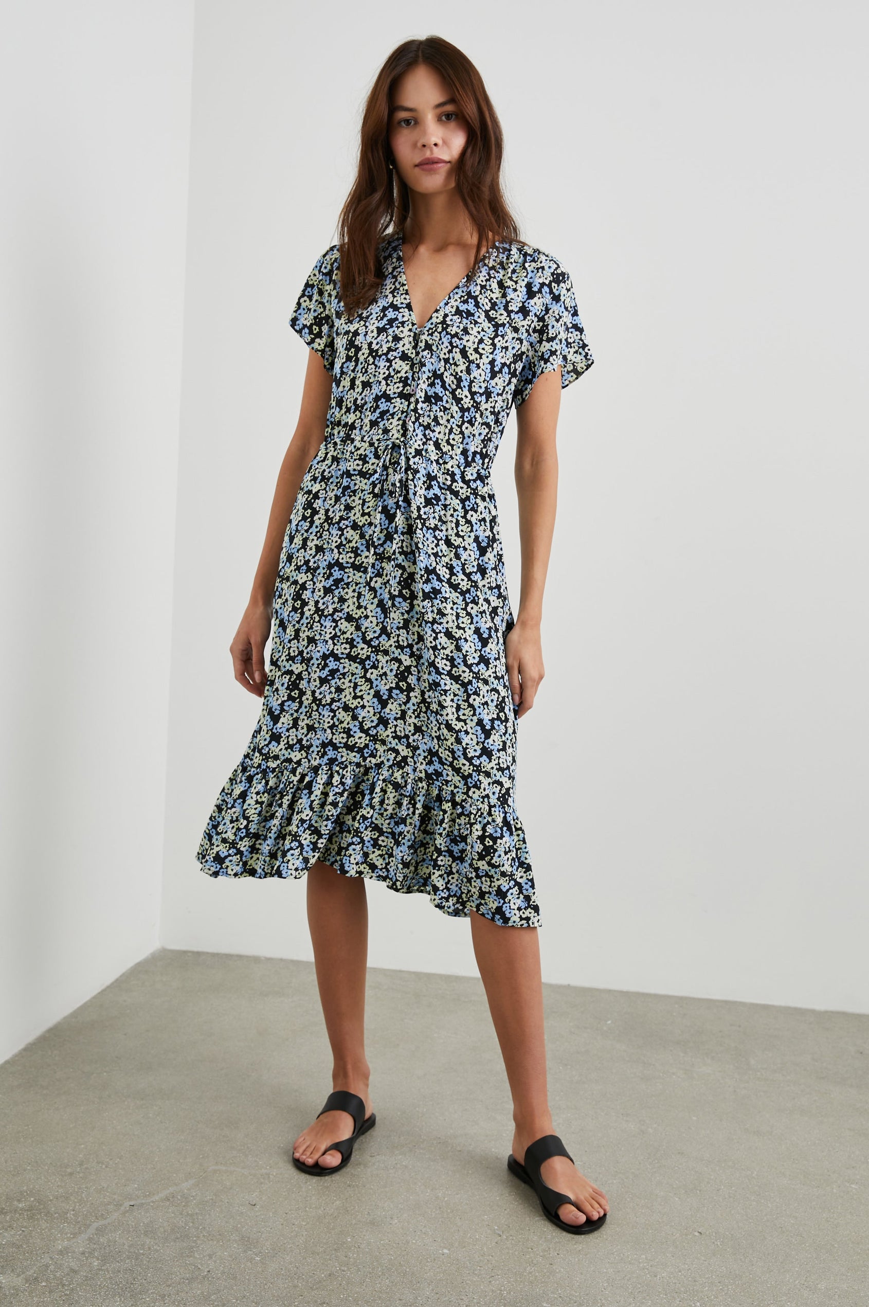 Kiki Short Sleeve Midi Dress with a V Neck, Buttons Down the Front Bodice, a Drawstring Waist and Ruffles at the Hem in Midnight Meadow Floral Colorway, Blue and Cream Flowers on Black - Front Full Body View Featured on Model
