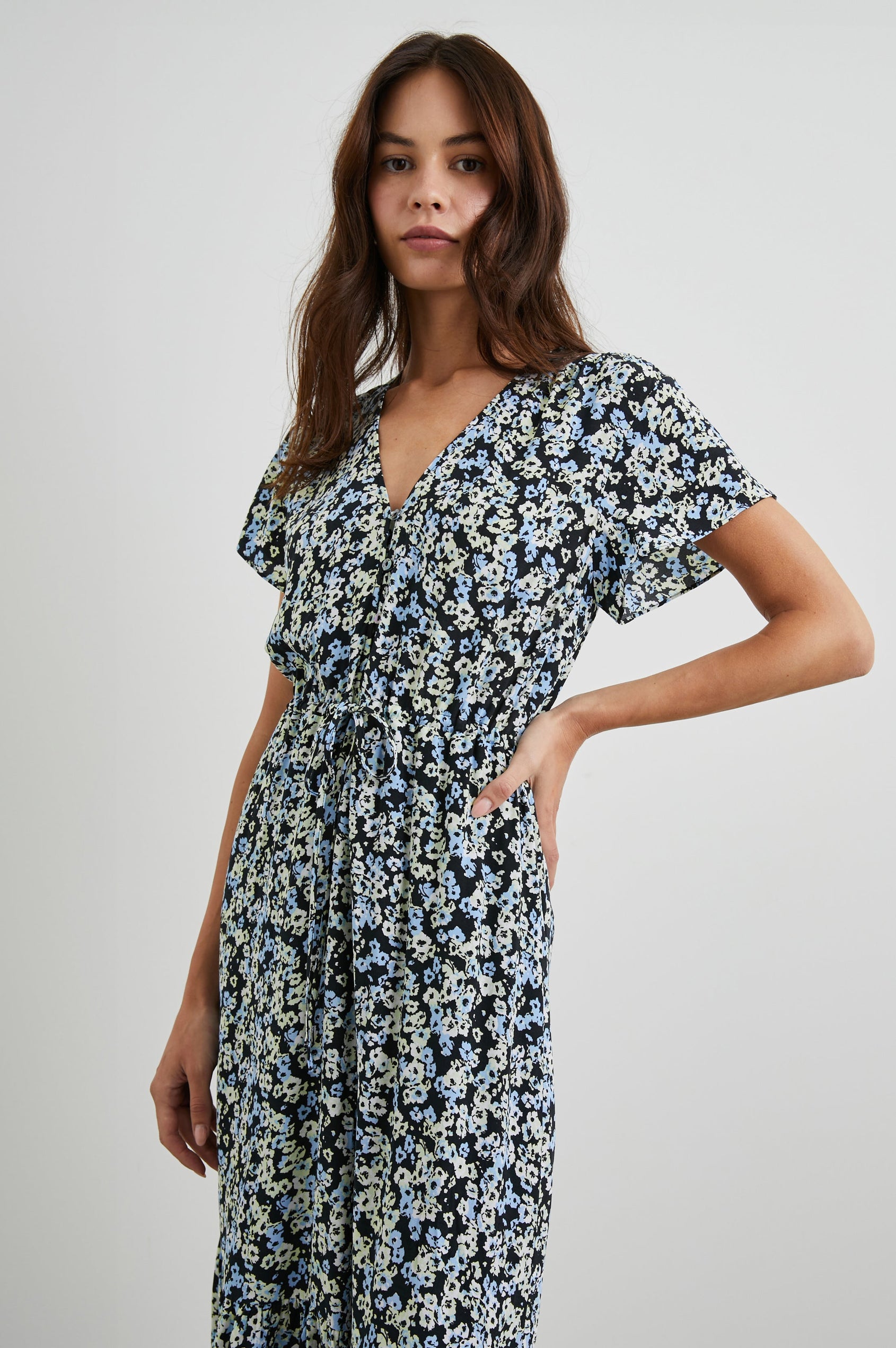 Kiki Short Sleeve Midi Dress with a V Neck, Buttons Down the Front Bodice, a Drawstring Waist and Ruffles at the Hem in Midnight Meadow Floral Colorway, Blue and Cream Flowers on Black - Front View Featured on Model