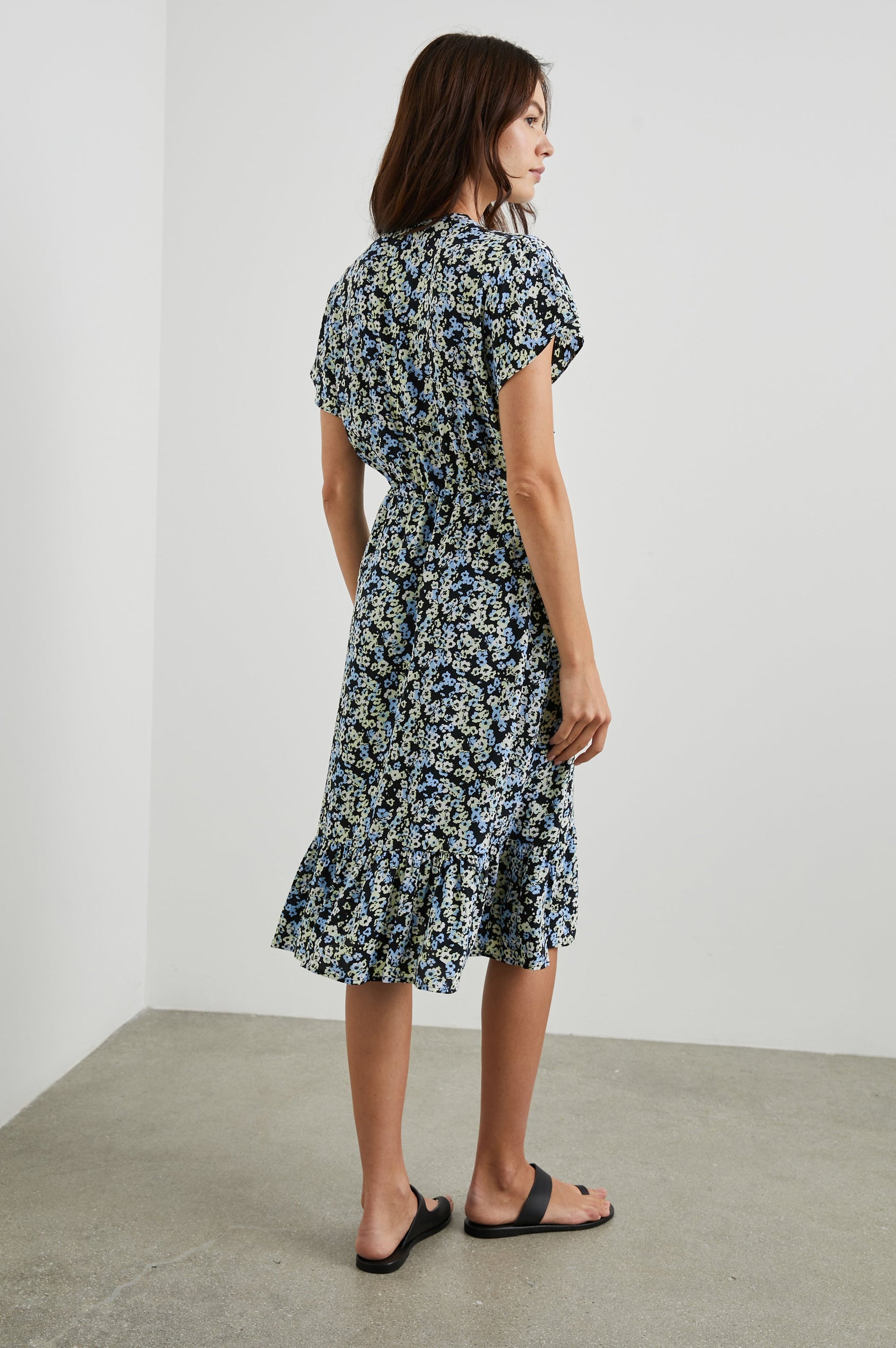 Kiki Short Sleeve Midi Dress with a V Neck, Buttons Down the Front Bodice, a Drawstring Waist and Ruffles at the Hem in Midnight Meadow Floral Colorway, Blue and Cream Flowers on Black - Back Full Body View Featured on Model