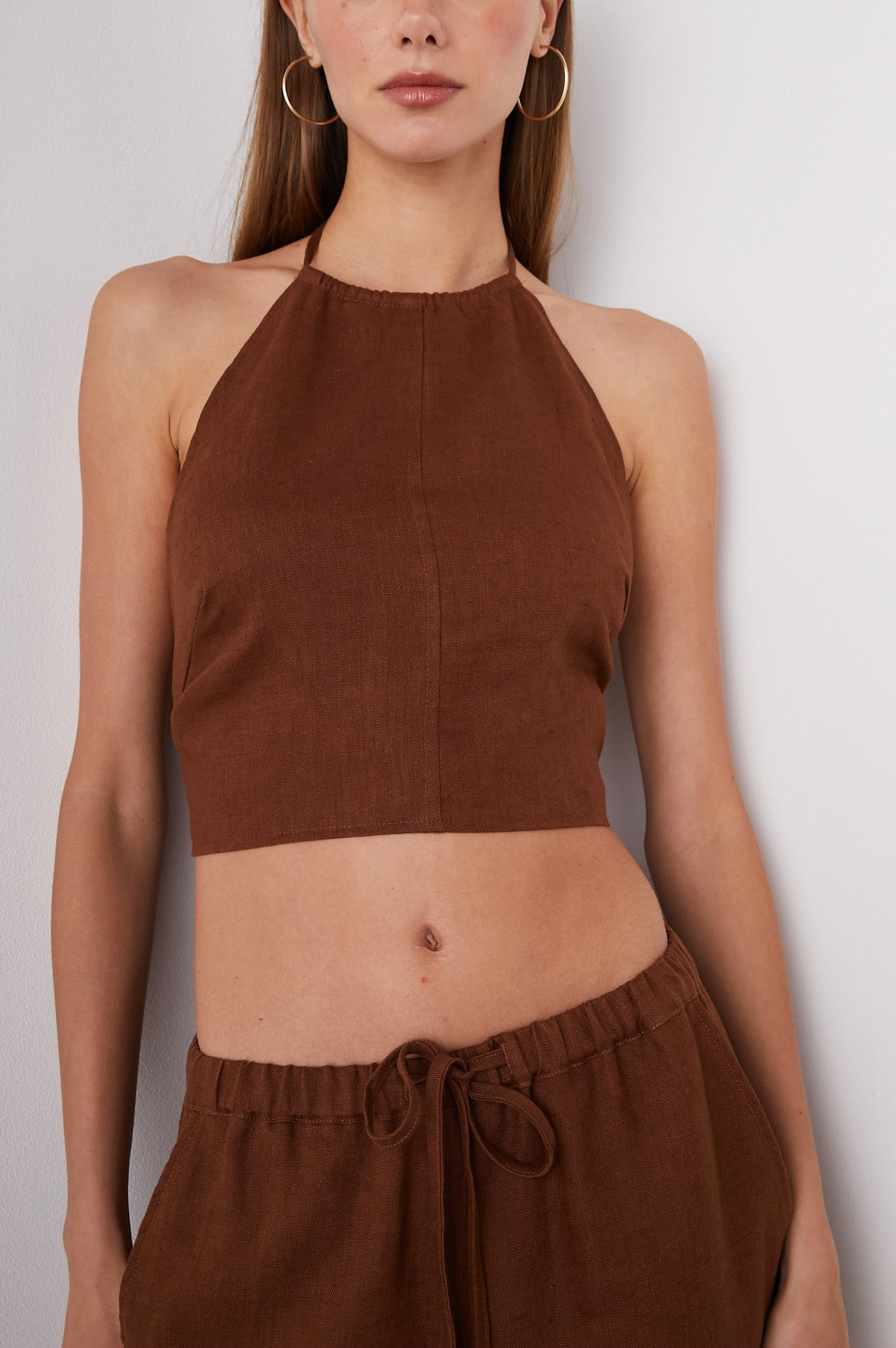 Kyra Sleeveless Crop Top with a Halter Neckline with a Back Neck Tie, an Open Back with Two Tie Closure and a Vertical Seam at the Front Center in Cacao Colorway - Front View Featured on Model