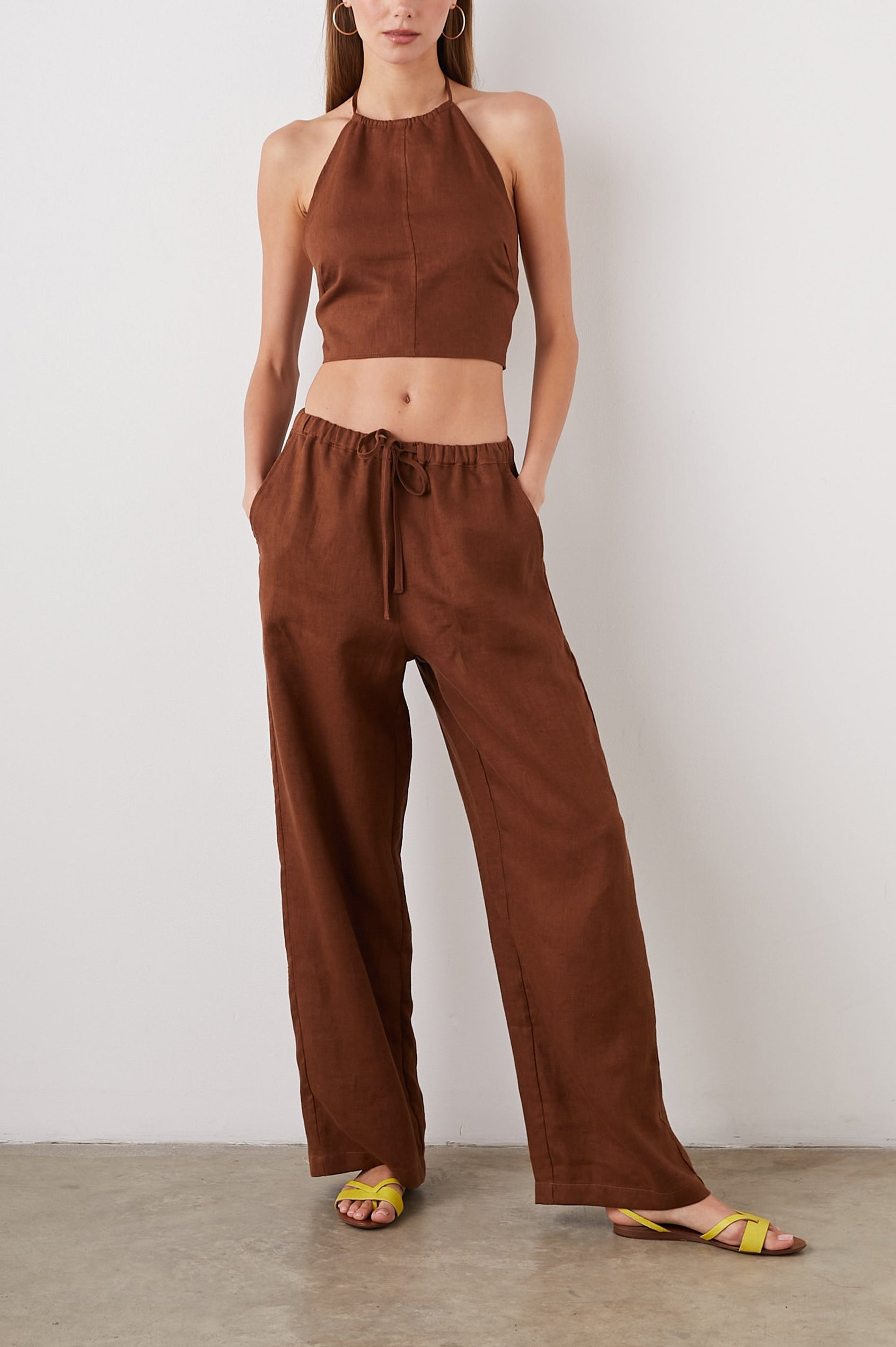 Kyra Sleeveless Crop Top with a Halter Neckline with a Back Neck Tie, an Open Back with Two Tie Closure and a Vertical Seam at the Front Center in Cacao Colorway - Front Full Body View Featured on Model