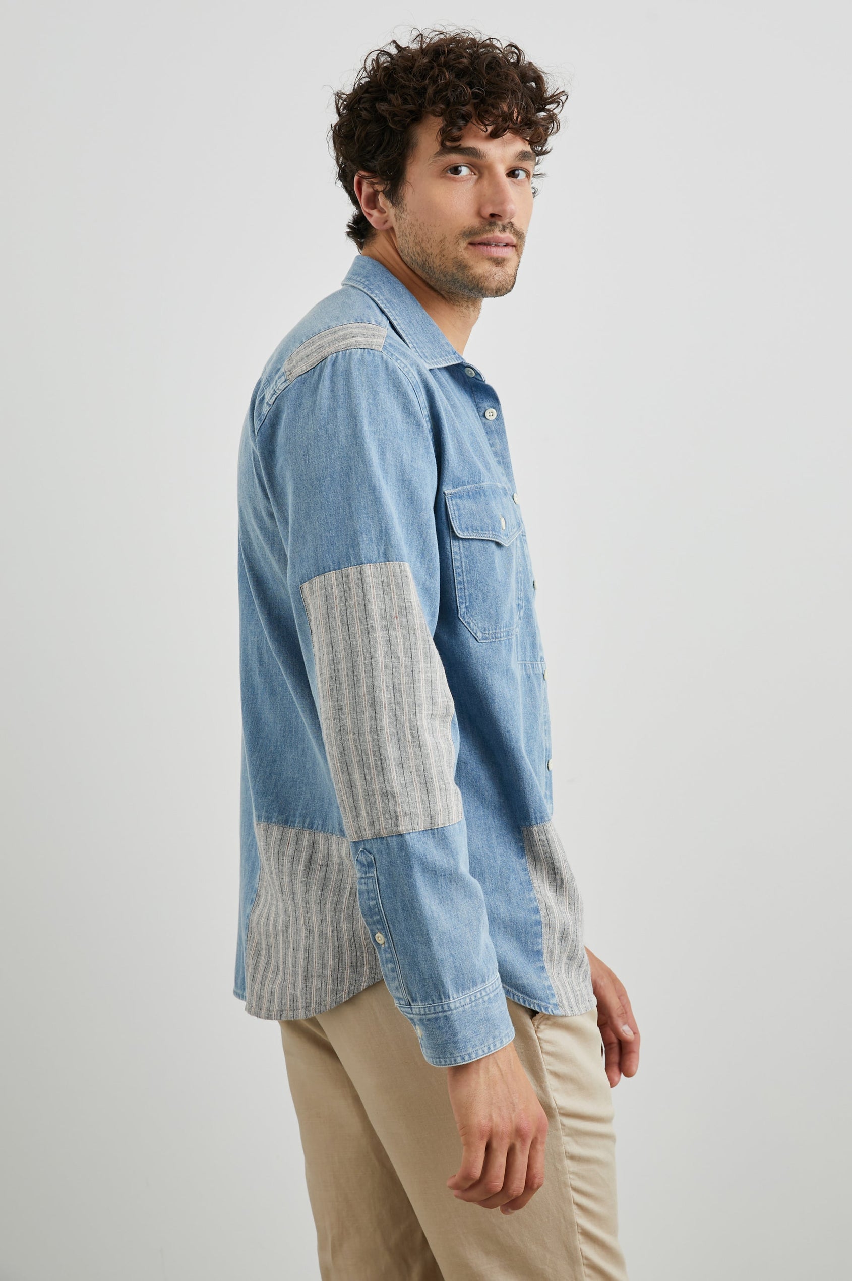 Larsen Long-Sleeve Button Up with Two Chest Button Flap Pockets in Medium Indigo Patchwork Colorway, Denim Patches and Vertical Stripes in Grey and White - Side Unbuttoned View Featured on Model