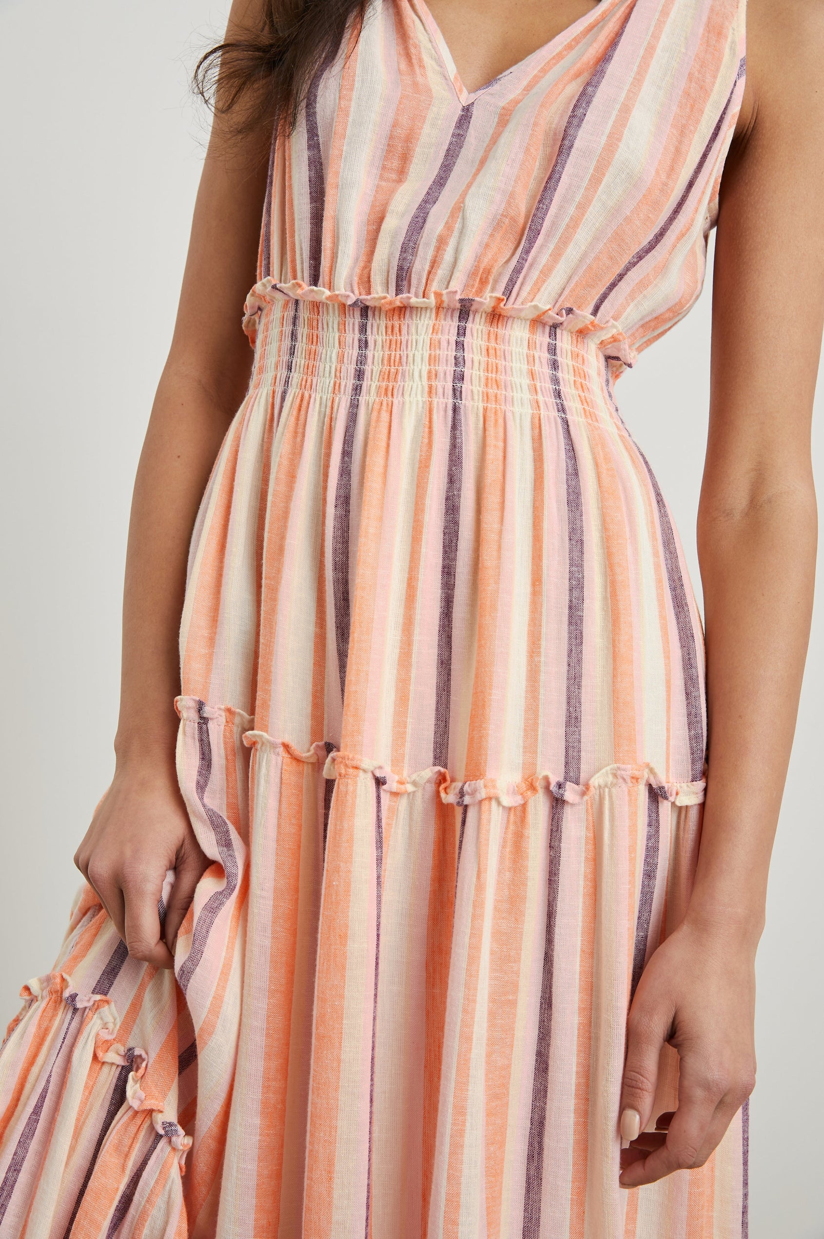 Loulou Sleeveless Midi Dress with a V Neck, Shirred Collar, Smocked Waist and Tiered Skirt in Papaya Stripe Colorway, purple, oranges and cream vertical Stripes - Front View Featured on Model