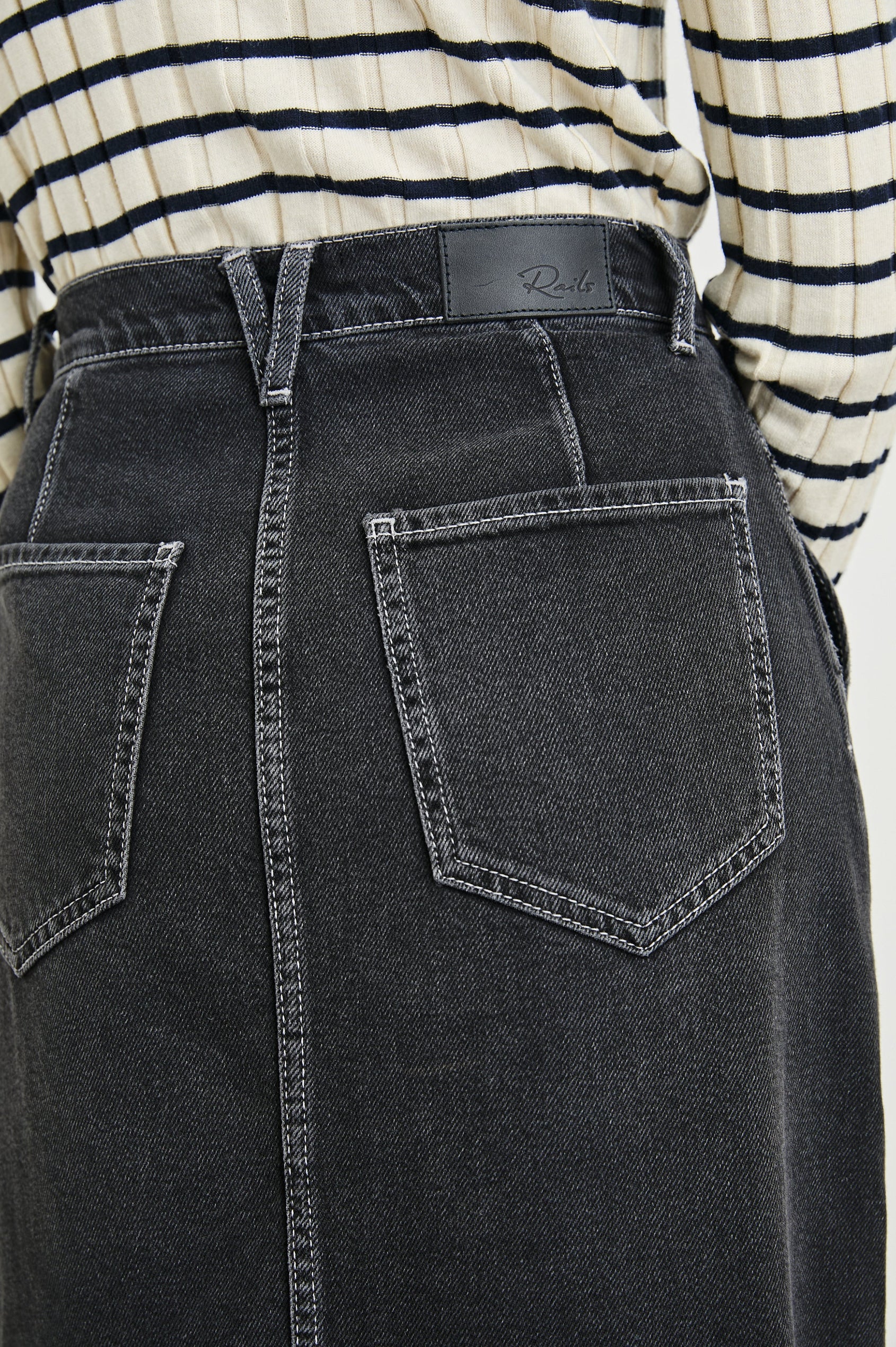 Manhattan Midi Denim Skirt with a Raw Hem, a Front Center Thigh Slit, Belt Loops, Two Front Pockets and Two Back Patch Pockets in Eclipse Colorway, a Black - Back View Featured on Model