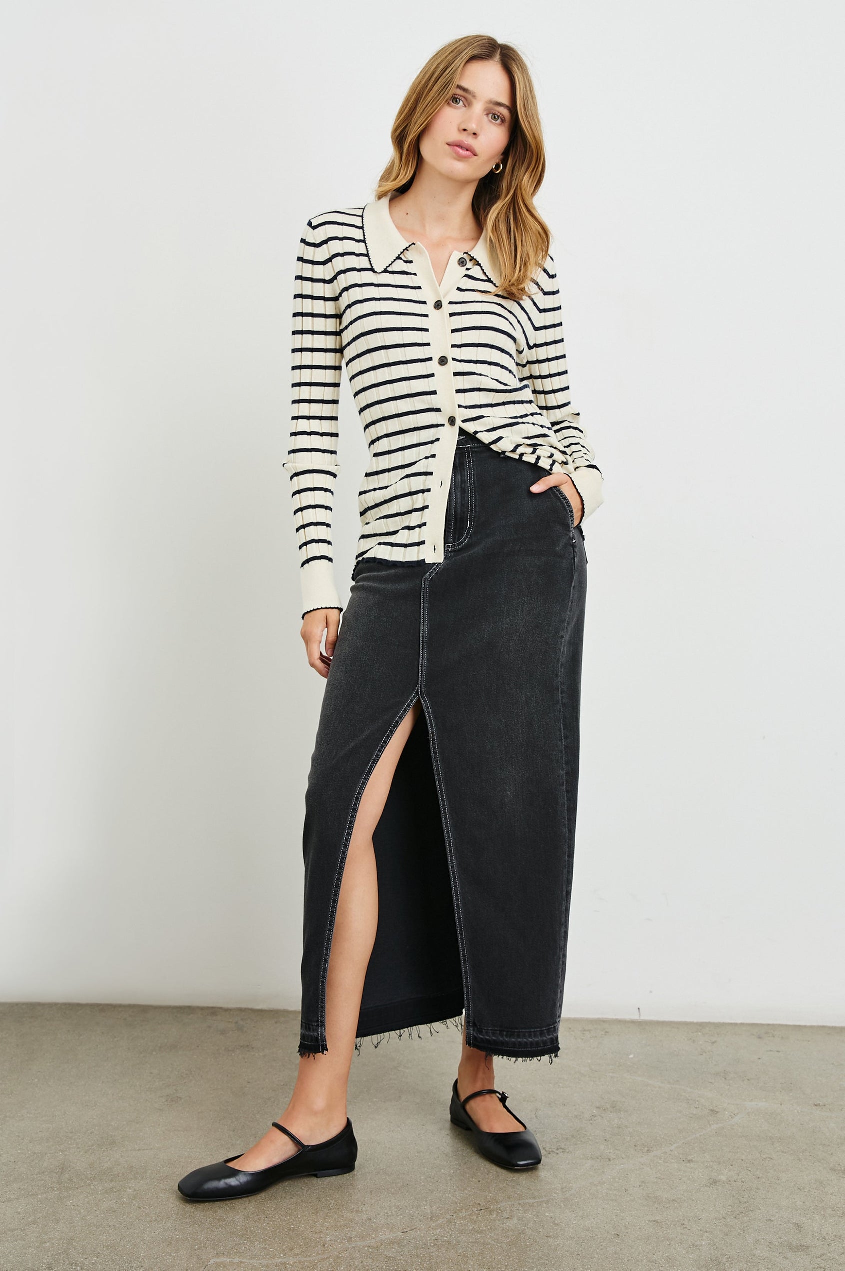 Manhattan Midi Denim Skirt with a Raw Hem, a Front Center Thigh Slit, Belt Loops, Two Front Pockets and Two Back Patch Pockets in Eclipse Colorway, a Black - Front Full Body View Featured on Model