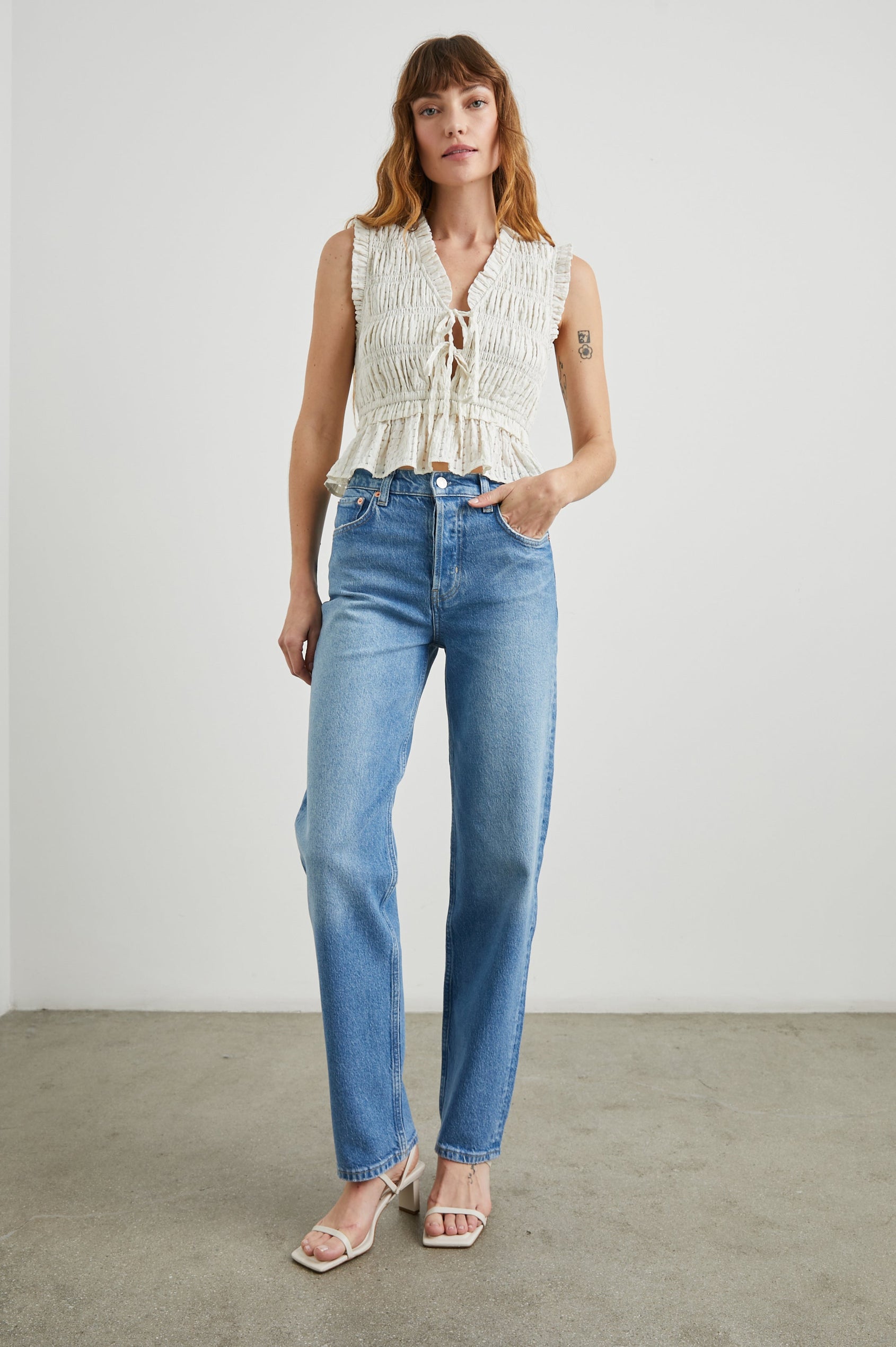 Martine Sleeveless Top with Ruffled Trim, a Deep V-Neck with Ties and Smocking in Ivory Seersucker Colorway - Front Full Body View Featured on Model