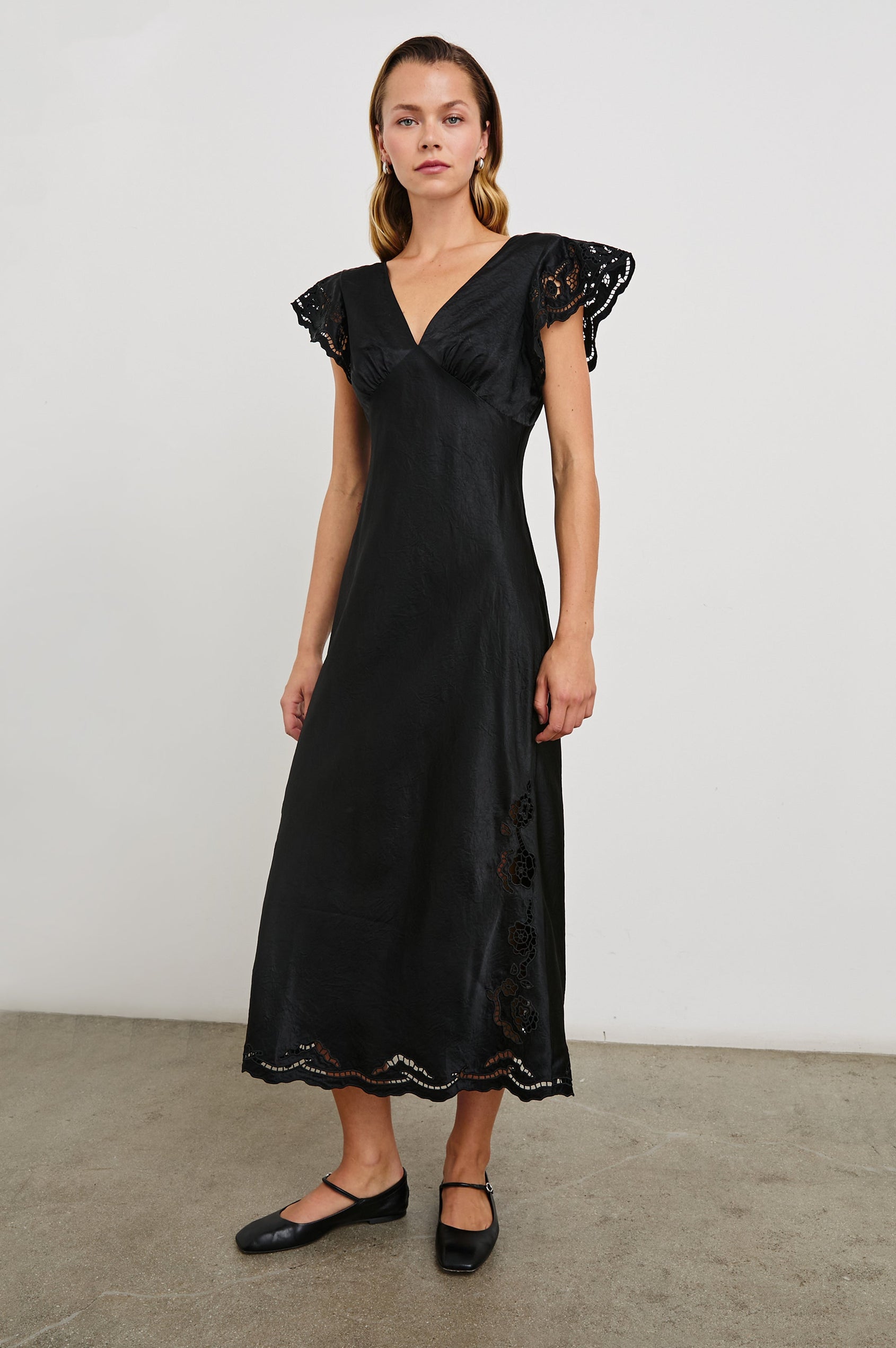 McKenna Short Sleeve Midi Dress with Flutter Sleeves, a Deep V Neck, an Eyelet Design on the Sleeves and Along the Hem and Floral Cutouts on the Skirt Sides in Black Eyelet Colorway - Front Full Body View Featured on Model
