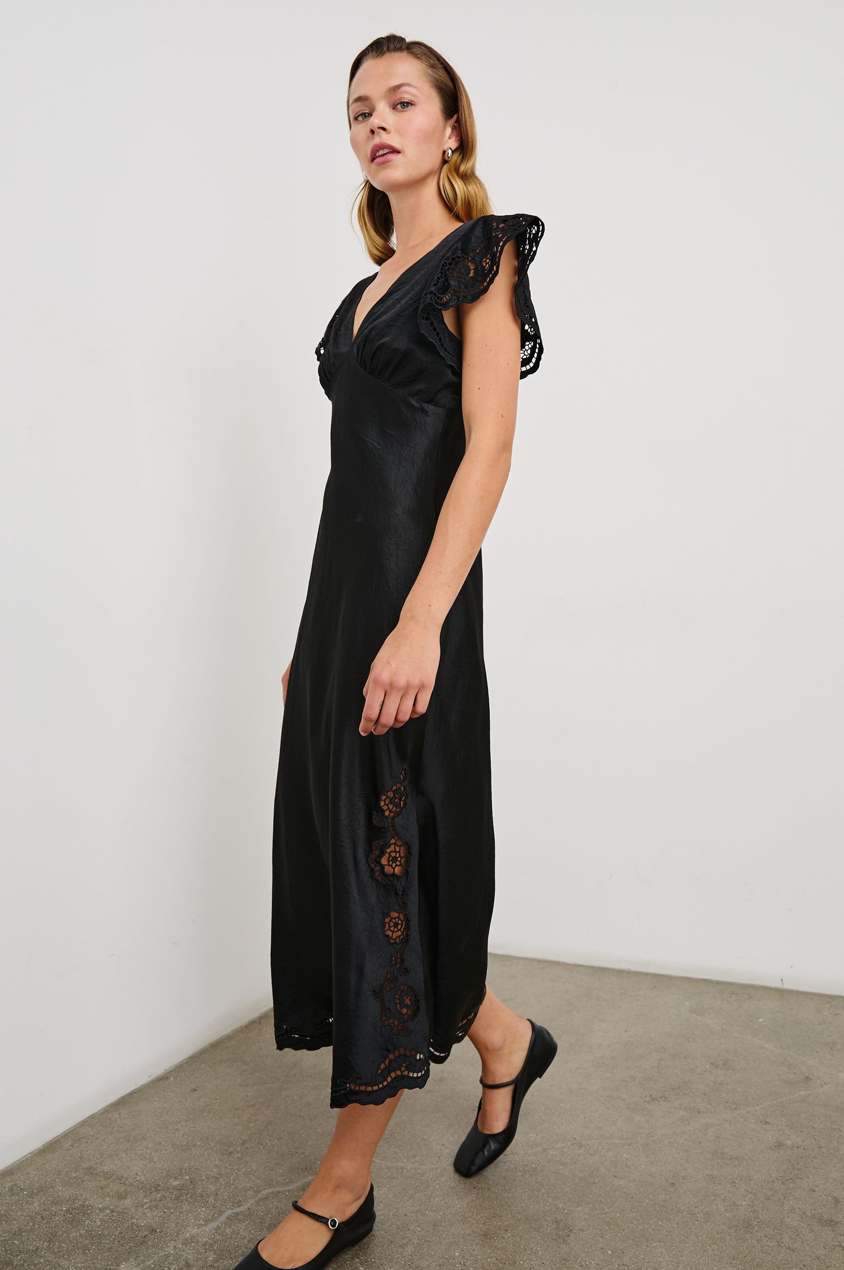 McKenna Short Sleeve Midi Dress with Flutter Sleeves, a Deep V Neck, an Eyelet Design on the Sleeves and Along the Hem and Floral Cutouts on the Skirt Sides in Black Eyelet Colorway - Front Full Body View Featured on Model