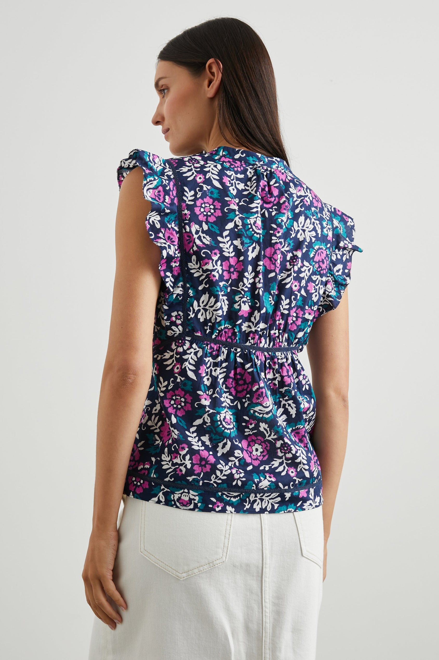 Misha Short Sleeve Top with Flutter Sleeves, a Deep V Neck, and Vertical and Horizontal Black Seams in Woodblock Floral Colorway, Pink, White and Green on Navy - Back View Featured on Model