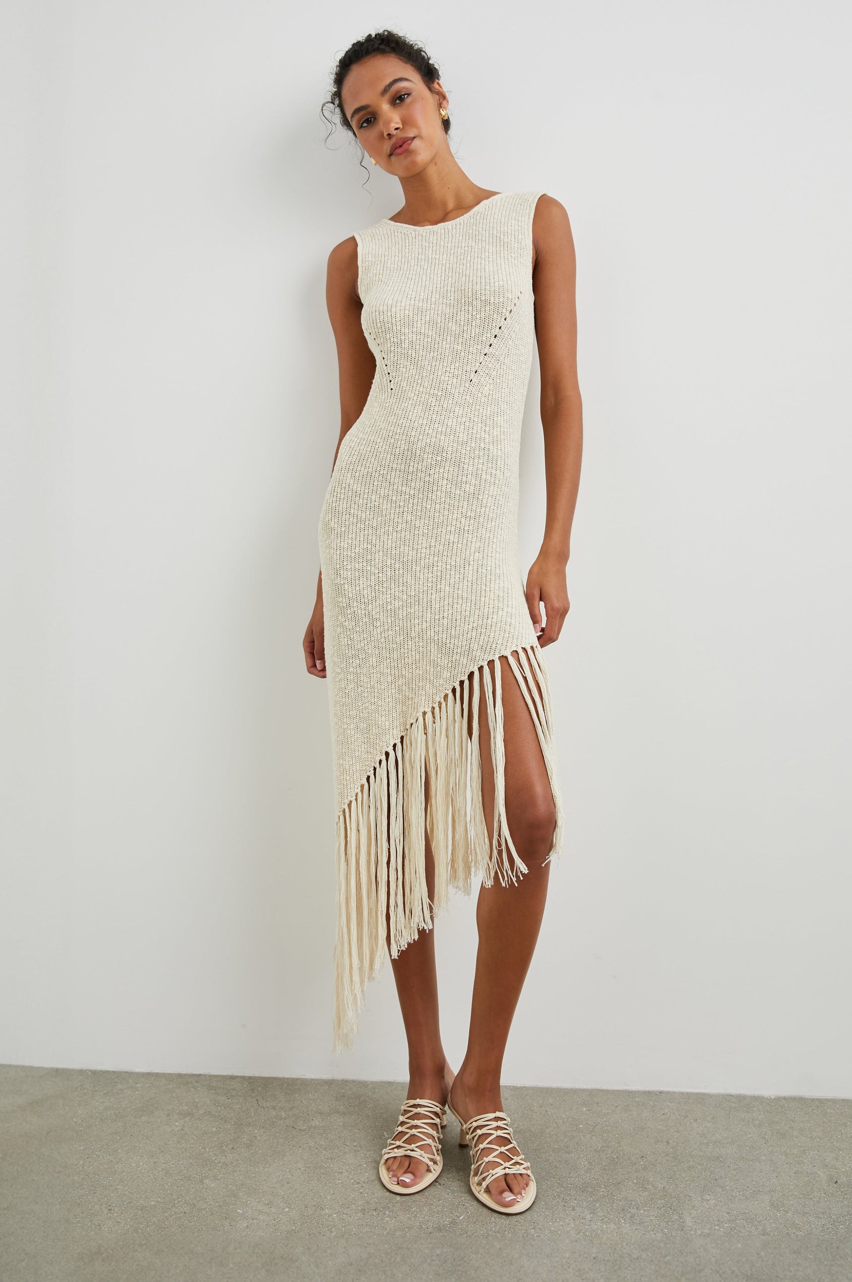 Rylee Sleeveless Ribbed Dress with a Scoop Neck, and a Fringed Asymmetrical Hemline from the Upper Thigh to the Knee in Ecru Colorway - Front Full Body View Featured on Model